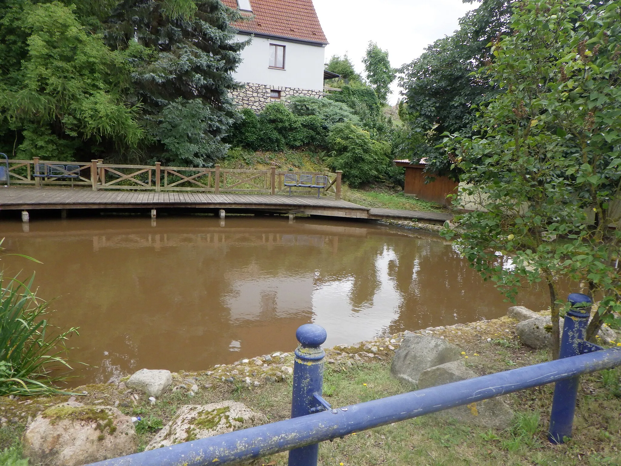 Photo showing: Der schon in der DDR-Zeit als Naherholungsgebiet genutzte Dorfteich wurde zum Ortsjubiläum 2018 in Kupfersuhl umgestaltet. Das Bild zeigt die teilweise überbaute Ostseite, dort wurde eine Art Bühne mit Sitzbänken und Laufsteg errichtet. Gelegentlich werden auch einige Petrijünger gesichtet, aber im Teich soll es nur kleine Fische geben.