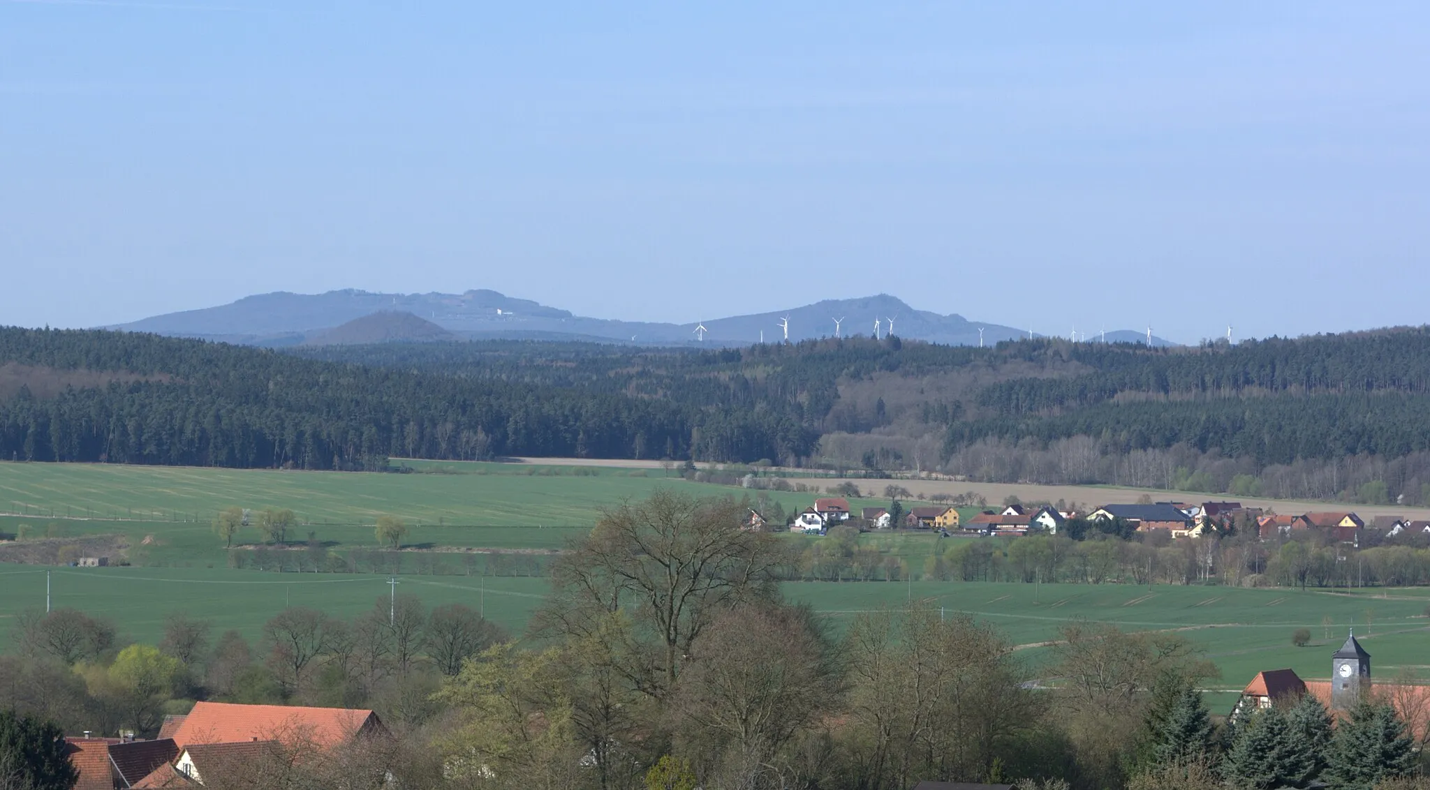 Photo showing: Blick von der „Trift“ am nördlichen Ortsrand Burkhardtrodas nach Südwesten über das Tal der Suhl (mit dem Lindigshof links dieser) zum Frauenseer Forst mit dem etwa 10 km entfernten dominanten Krayenberg. Dahinter sind in etwa 20 km Entfernung mit Dietrichsberg und Öchsen erste Kuppen der Rhön zu sehen. Am rechten unteren Bildrand sieht man die ehemalige Dorfschule mit  Uhrenturm.