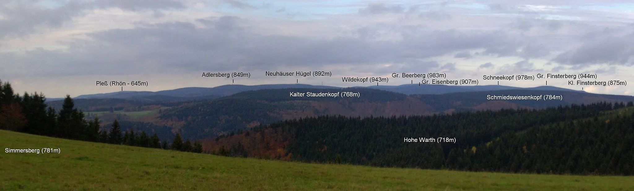 Photo showing: Blick vom Simmersberg (781 m) auf die höchsten Berge des Thüringer Waldes: Adlersberg (849 m) mit Neuhäuser Hügel (891 m), Großer Beerberg (teils verdeckt, 983 m), Wildekopf (943 m), Großer Eisenberg (907 m), Schneekopf (978 m), Großer (944 m) und Kleiner (875 m) Finsterberg; im Vordergrund Kalter Staudenkopf (768 m) und Schmiedswiesenkopf (784 m) - der Große Riesenhaupt (764 m) bei Frauenwald und der Große Hundskopf (824m) bei Allzunah schlössen sich rechts an - sowie der Nebengipfel Hohe Warth (718 m);  links im Hintergrund der 52 km entfernte Pleß (645 m) in der Vorderen Rhön