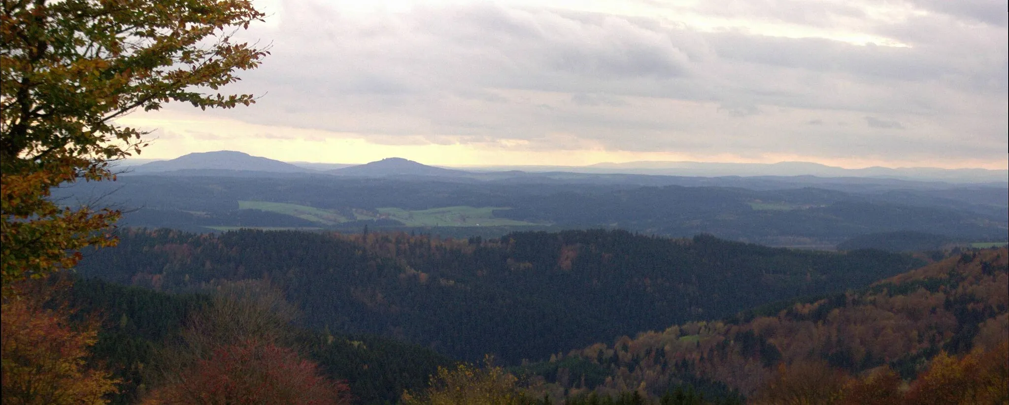 Photo showing: Blick vom Simmersberg (781 m) im Thüringer Schiefergebirge auf die 24 km entfernten Gleichberge (679 und 641 m). Rechts im Hintergrund die Hohe Rhön mit dem 67 km entfernten, 928 m hohen Kreuzberg, unmittelbar davor (halbrechts mittig) der 7 km entfernte Ratscher Bergsee. Im Vordergrund der 621 m hohe, nur 3 km entfernte Wachberg