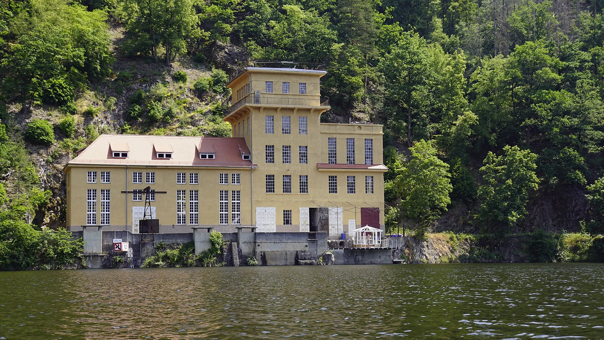 Photo showing: Altes Wasserkraftwerk am Hohenwartestausee bei Ziegenrück, von 1918, welches nach dem Talsperrenbau in den 1940er-Jahren außer Betrieb genommen wurde. Auf der anderen Seite des Berges wurde der Saale Wasser entnommen, durch einen Tunnel im Berg in dieses Wasserkraftwerk geleitet und dort wieder der Saale zugeführt.