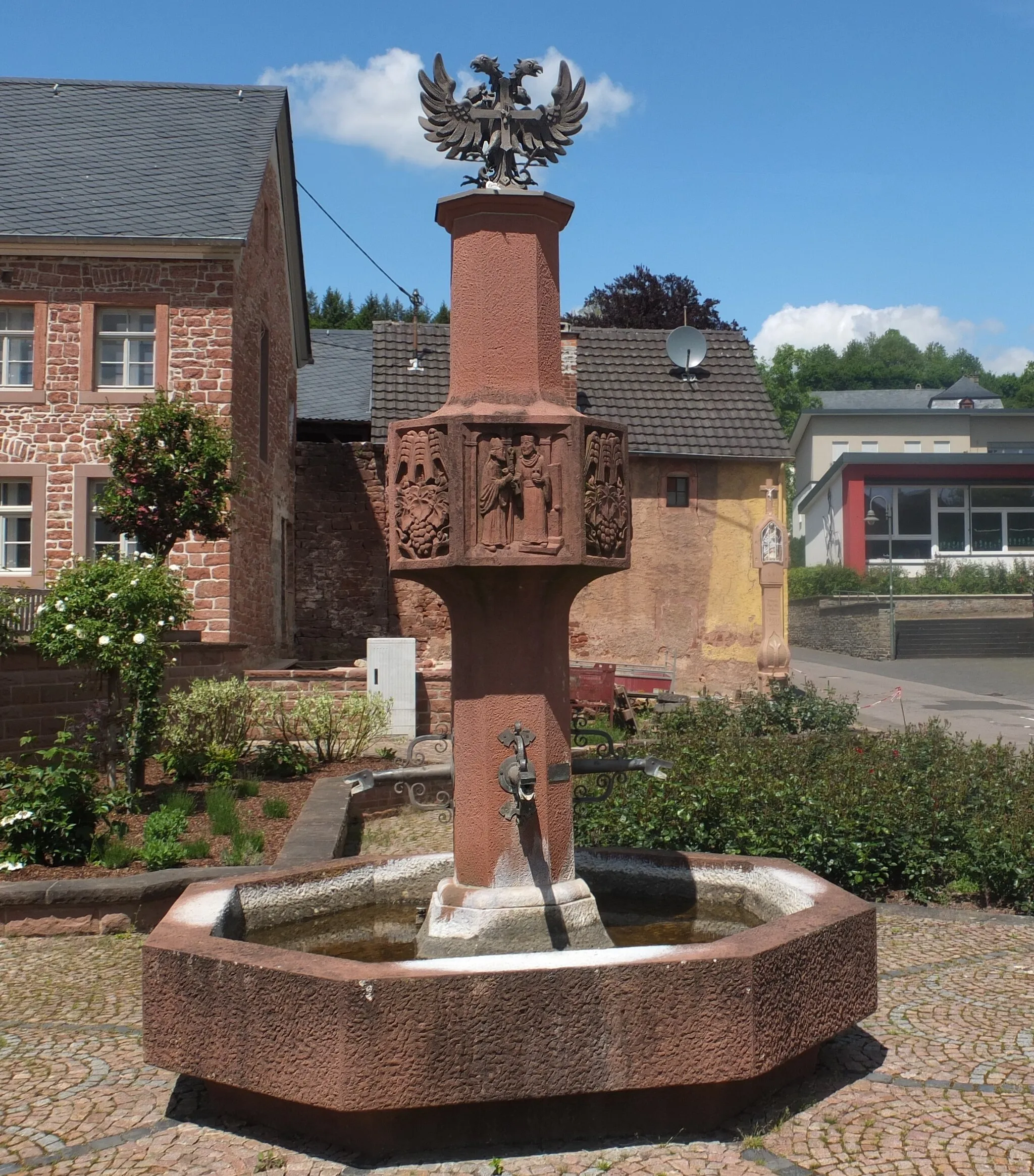 Photo showing: Village fountain and so-called Prangerkreuz in the background, Dreis, Rhineland-Palatinate.
