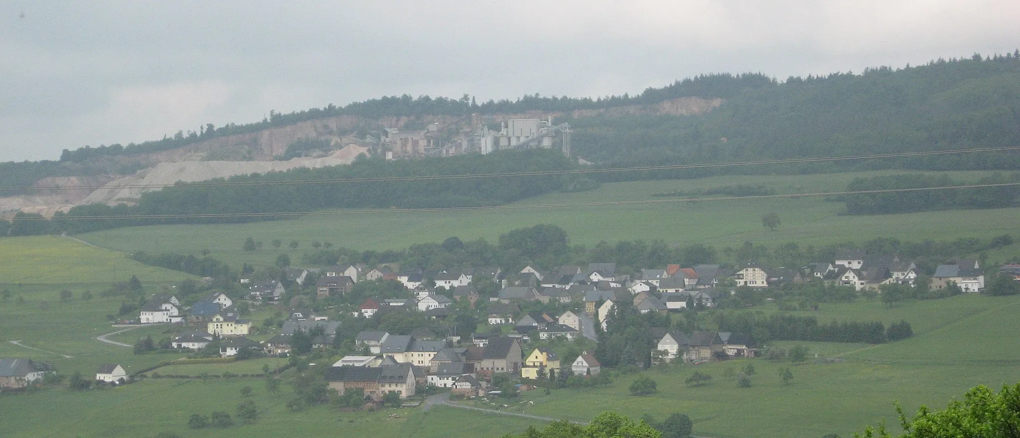 Photo showing: Village Henau in the Hunsrück landscape, Germany; behind the village a Quarry at the southwestern edge of Koppensteiner Höhe