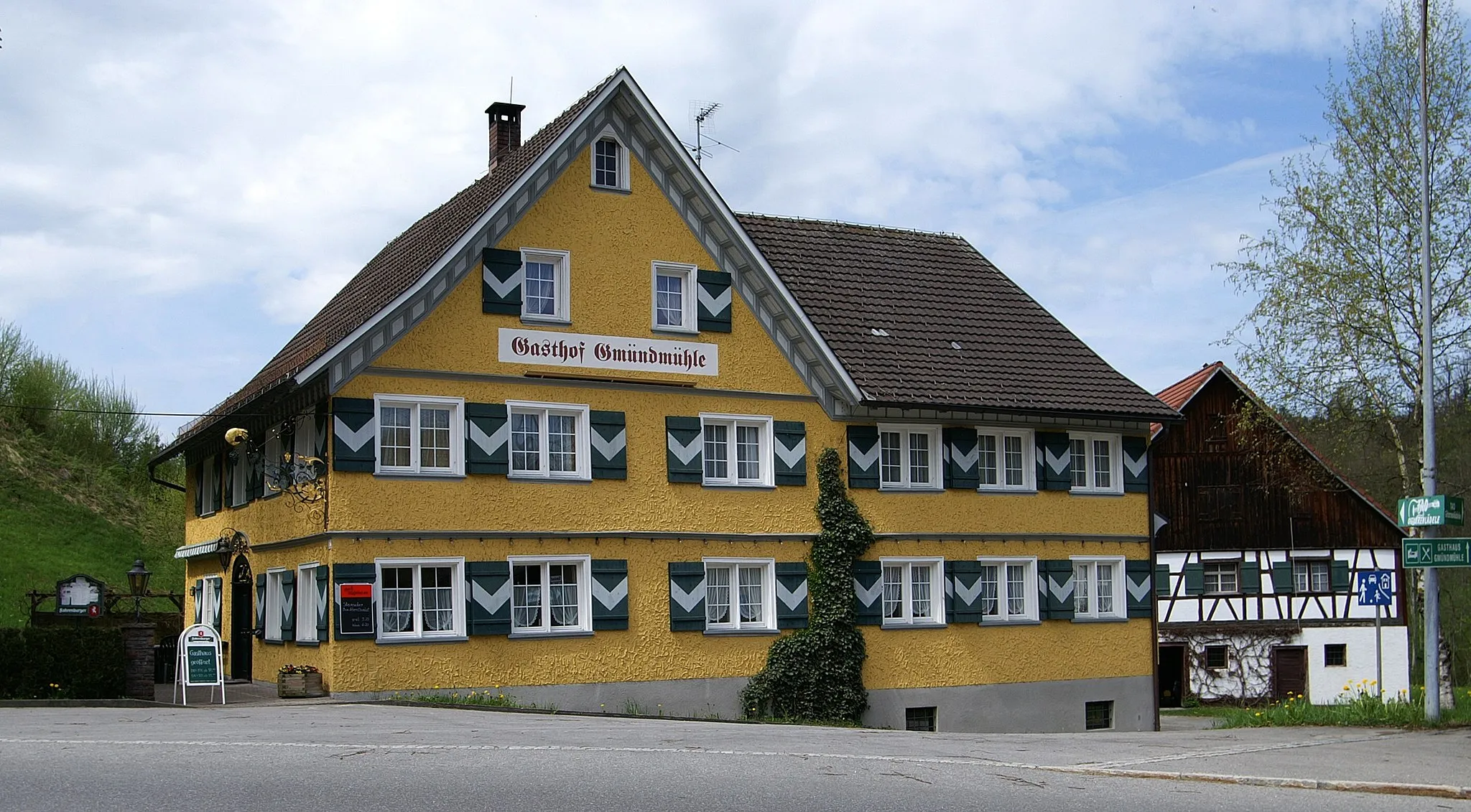 Photo showing: aus dem DEHIO Vorarlberg 1983: Hohenweiler, Gmundmühle mit Gasthaus Traube: Im Weiler Gmünd an der Staastgrenze, 2geschossiger Bau mit Giebelgeschoß und Kreuzgiebel, 2 Giebelfassaden mit Klebdächern, korbbogiges Portal mit klassizistischen Oberlichtgittern, bezeichnet 1815, schmiedeisener Ausleger 2. Hälfte 18. Jh. Rückseitig 2armige Freitreppe, darunter Kellerportal mit Steingewände, bezeichnet 1743. Daneben Wirtschaftsgebäude - Stall - Tenne - Schopf, Wohnteil in Fachwerk, traufseitiger Eingang im Obergeschoß, Tennentor mit Ochsenblutbemalung, Stadellukenbretter (Herzformausschnitte), gemauerte Ställe. *** in Vorarlberg