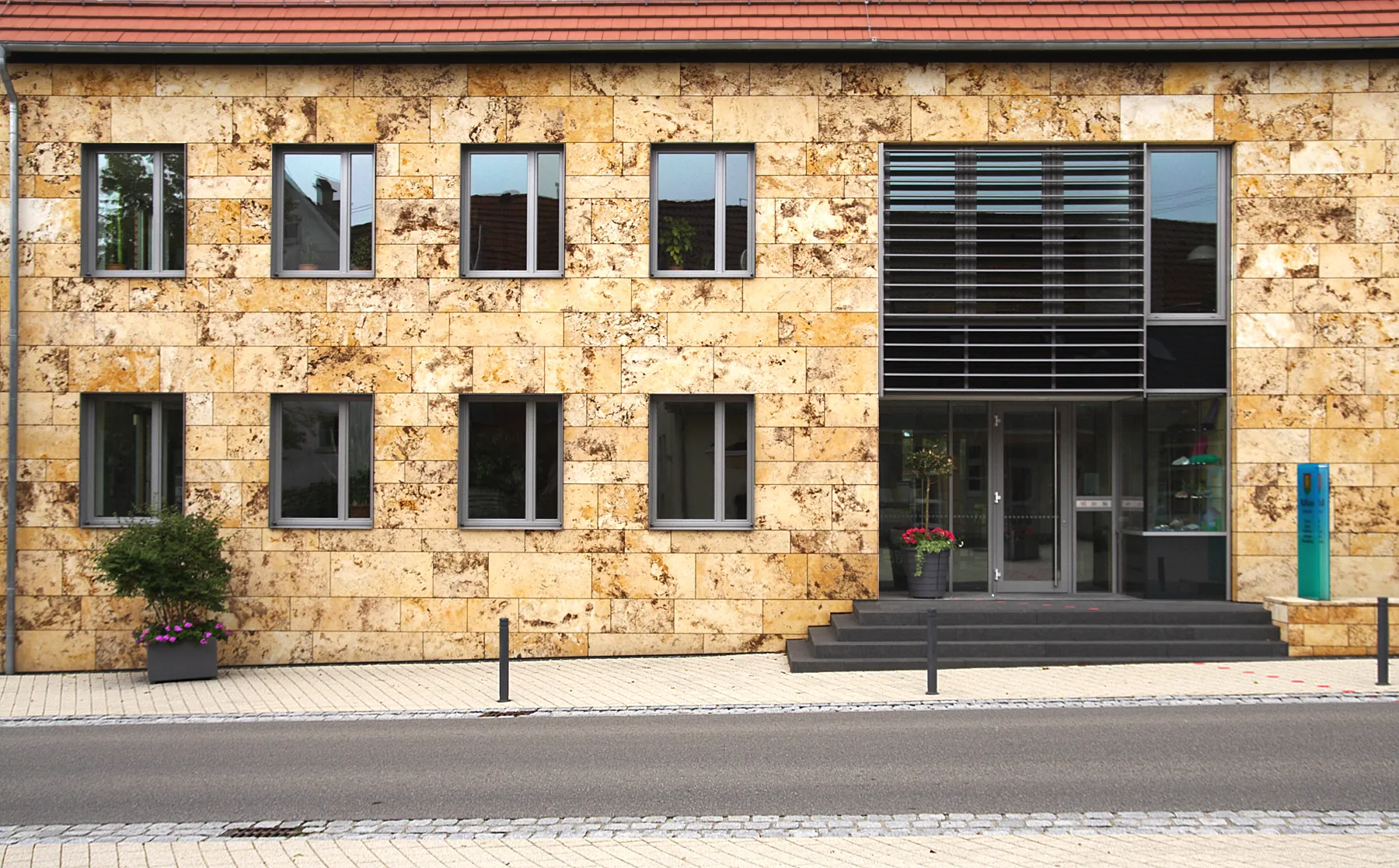 Photo showing: Hohensteins new town hall is covered with plates of travertine, a karst product, sedimented in turbulent river sections and behind huge karst springs. When wet, travertine can easily be sawn. The dry material is extremely consolidated and weatherproof. The cavities and impurities - remnants of debris and biotic materials - make the plates very decorative and yet porous and thus lightweight.