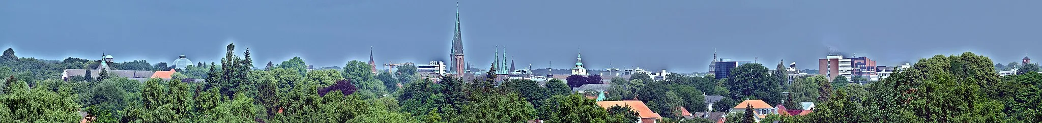 Photo showing: Downtown Oldenburg, viewed from the "Osternburger Utkiek" park: On the left, the roof of the district court [Amtsgericht] as well as the water tower "Alte Fleiwa" (a former meat processing plant) and the cupola the State Theater [Staatstheater] can be seen. In the middle, the towers of St Peter's Church, St Lambert's Church, and the palace are visible as well as the tower of the train station on the far right.