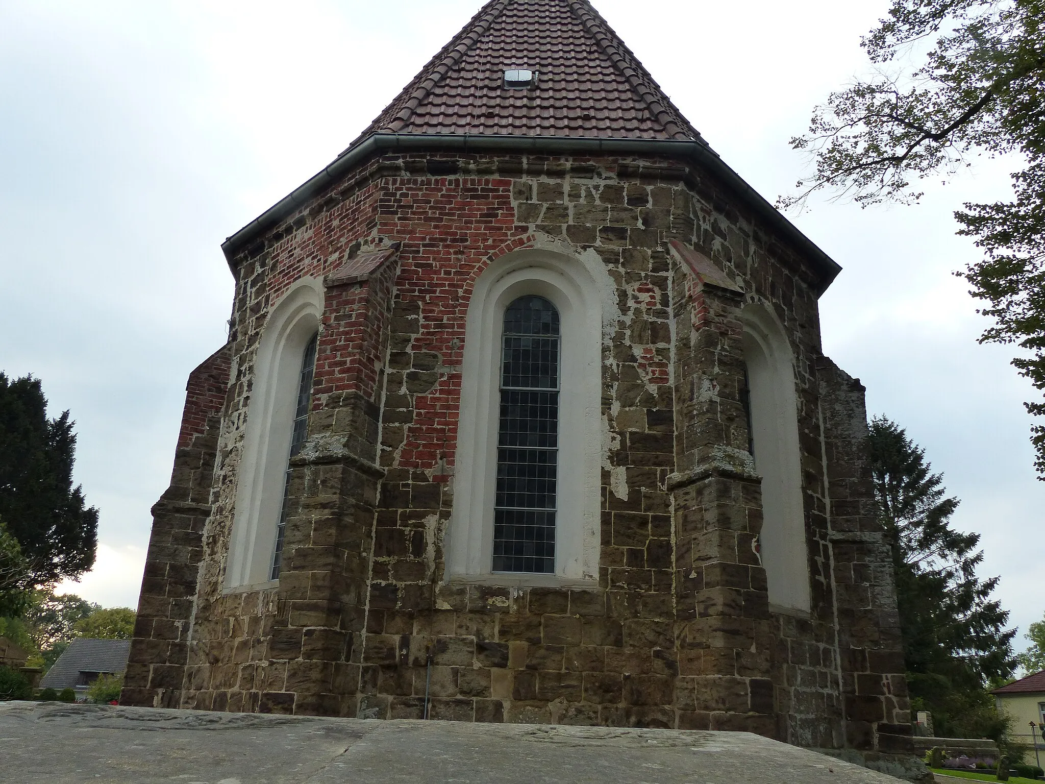 Photo showing: Matthäuskirche Esenshamm, polygonale Apsis mit Strebepfeilern, Fenster Rundbögen mit Übergang zum Spitzbogen, insbes. beim halb mit Backstein reparierten Scheitelfenster
