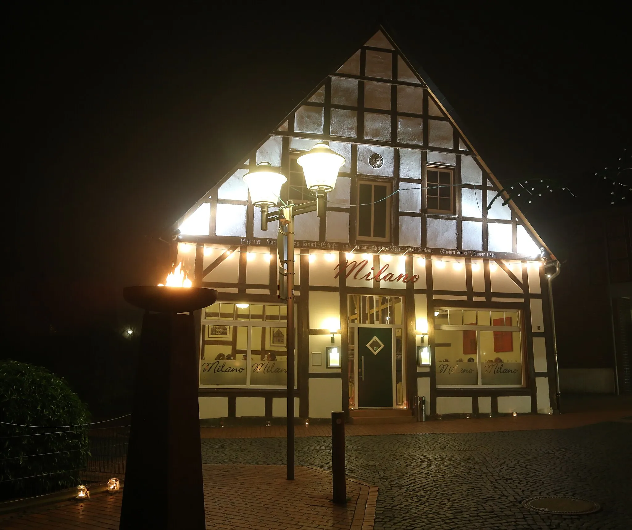 Photo showing: The restaurant Milano in the city centre of Westerkappeln, Kreis Steinfurt, North Rhine-Westphalia, Germany. The timber framed building and streets were illuminated on the occasion of the Moonlight Shopping event.