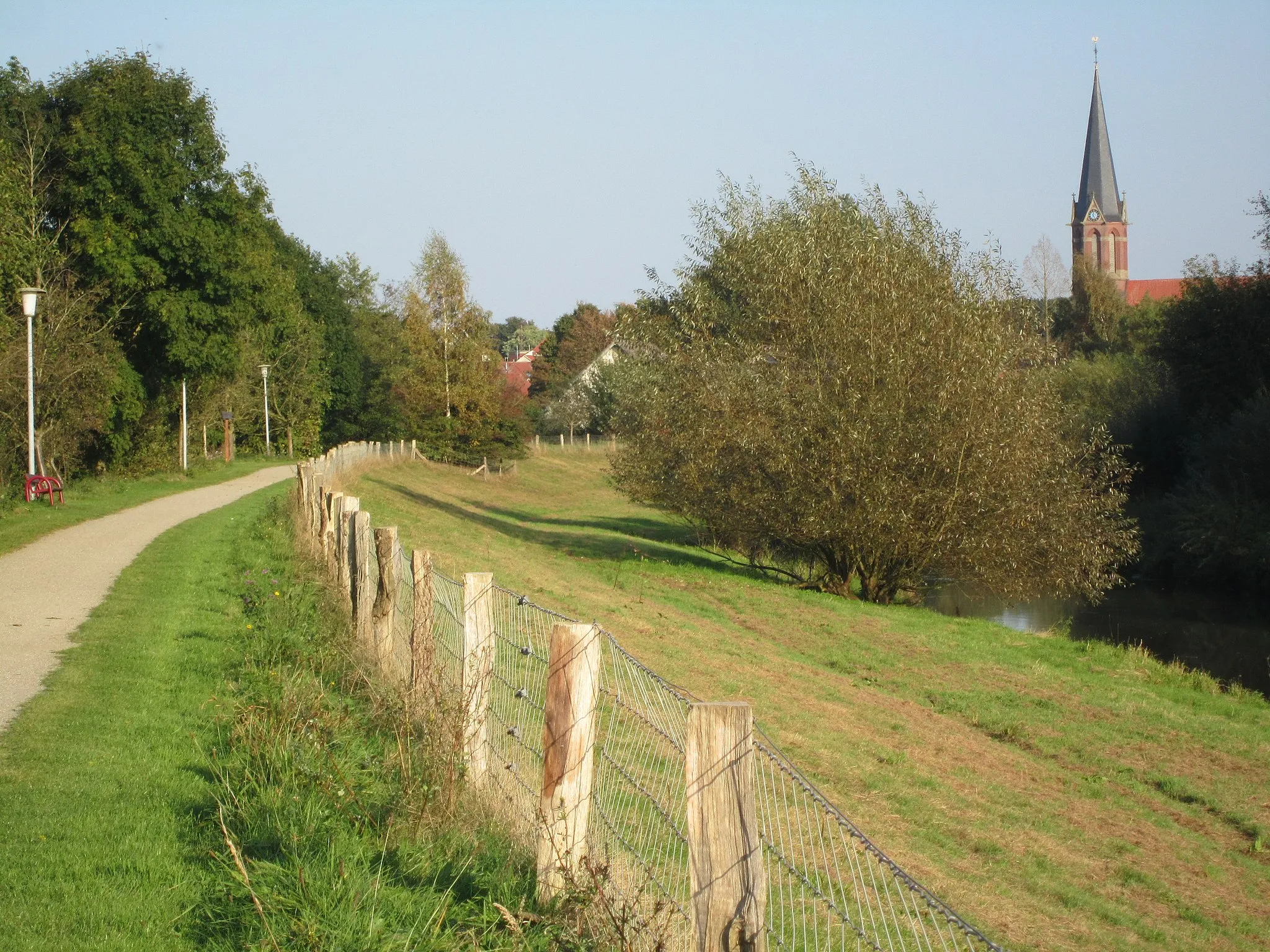 Photo showing: Bank of the Lager Hase near Essen in Oldenburg; on the left side the "Hase-Ems-Tour" (far distance bikeway), in the background the roman catholic parish church St. Bartholomäus