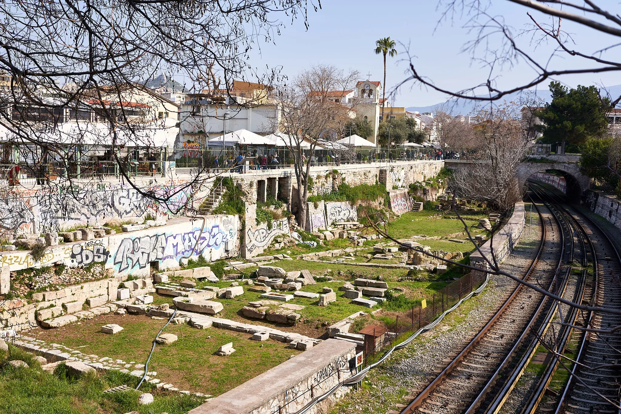 Photo showing: View of the recently excavated part of the Ancient Agora of Athens, between the train line and Adrianou Street, from a bridge near the Temple of Hephaestus. On the upper right corner of the picture, the Stoa of Attalus. The bridge in the distance leads to the entrance of the archaeological site of the Ancient Agora. Athens, Greece.