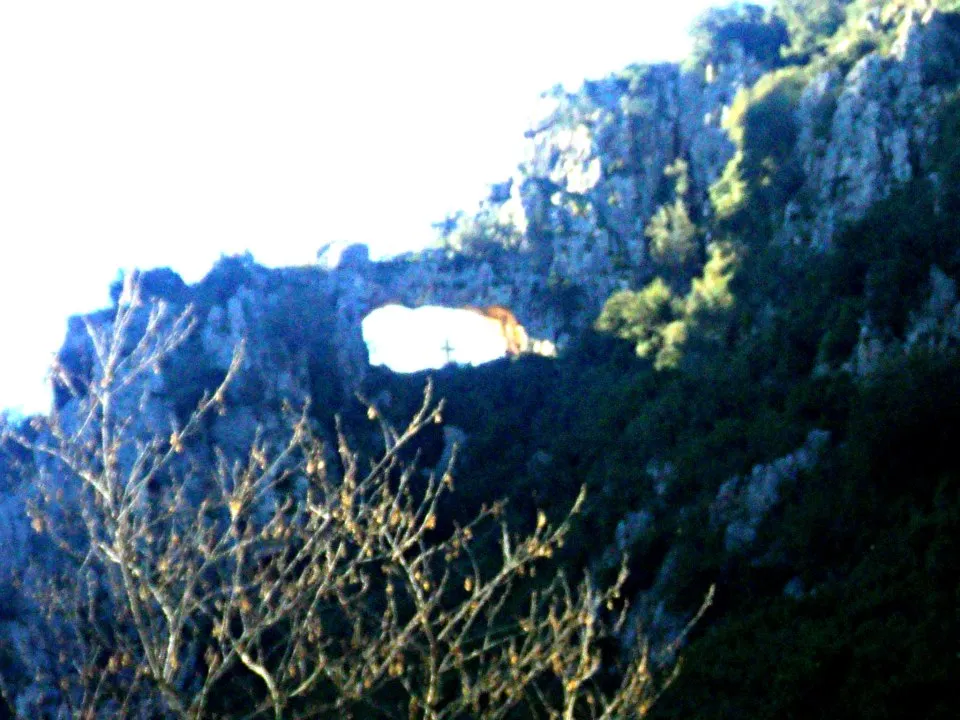 Photo showing: Βραχώδες βουνό σε μορφή τείχους, με τρύπα που το διαπερνά ώστε να είναι ορατή και από τις δύο πλευρές. Στο κέντρο της ένας σταυρός.