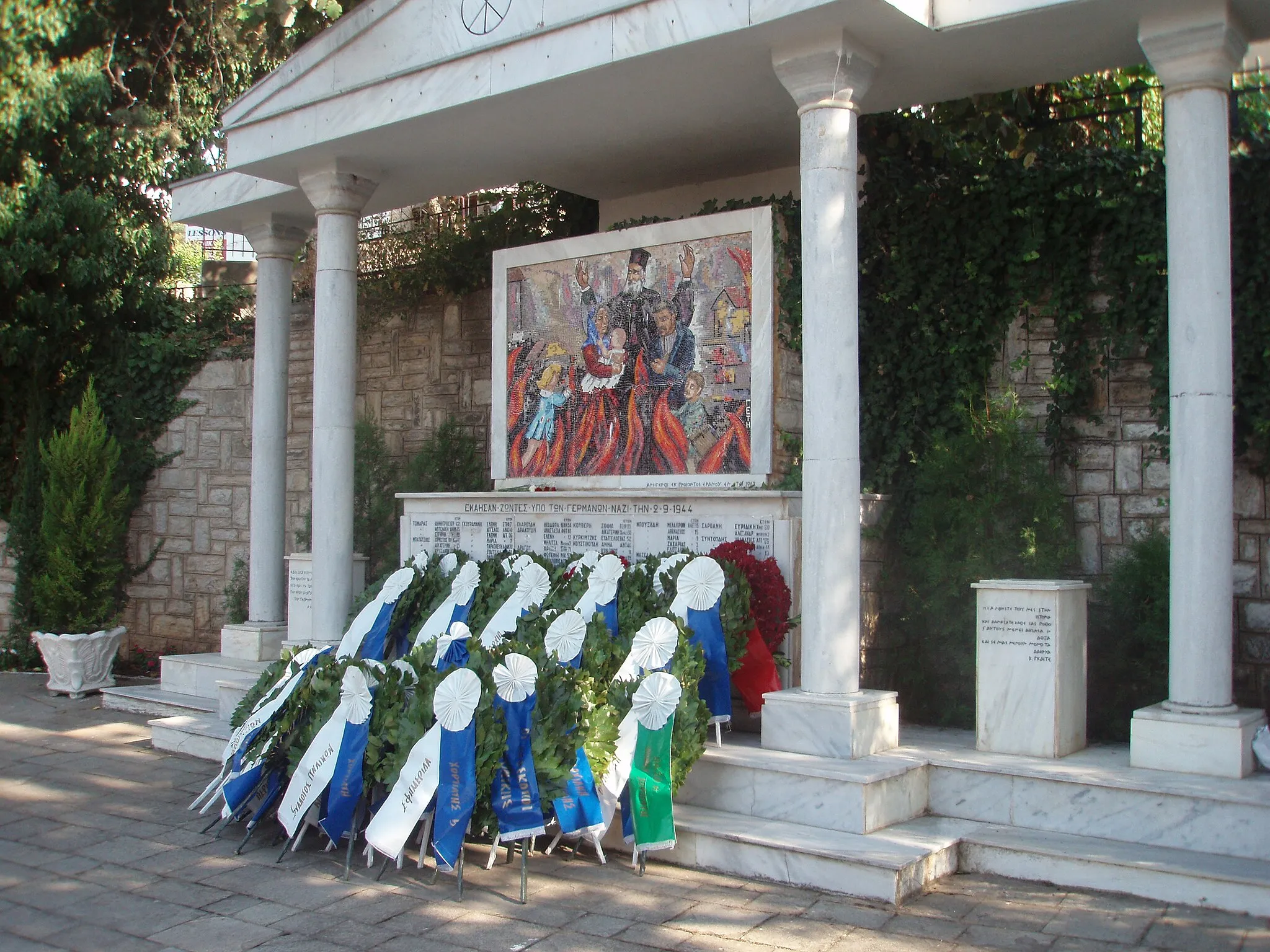 Photo showing: Memorial for the massacre of Chortiatis, Thessaloniki prefecture, Region of Central Macedonia, Greece. The massacre was committed on September 2nd, 1944 by German occupation troops and Greek collaborating forces and caused 149 people of the village Chortiatis to succumb. Picture was taken one day after memorial service with lying wreaths beside memorial, including one of the German General Consul in Thessaloniki.