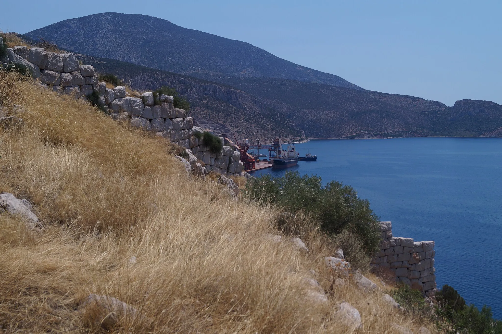 Photo showing: Medeon, Boeotia, Greece: Classical city wall on the west side of the Acropolis. In the background there is the Agios Spyridon port of Aluminium de Grece.