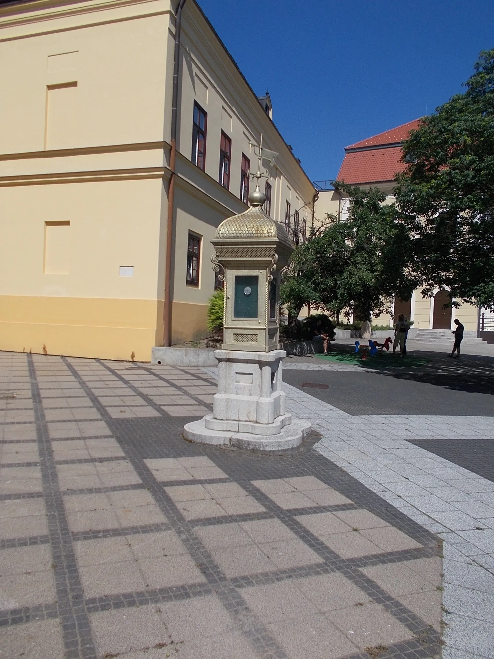 Photo showing: Weather station 'house' (column). Built in 1913 ordered by the ~1st City 'Architecture' Association. Renovated in 1983 by the ~1st City 'Architecture' Association At back the elementary school - Kossuth Square, Kaposvár, Somogy County, Hungary.