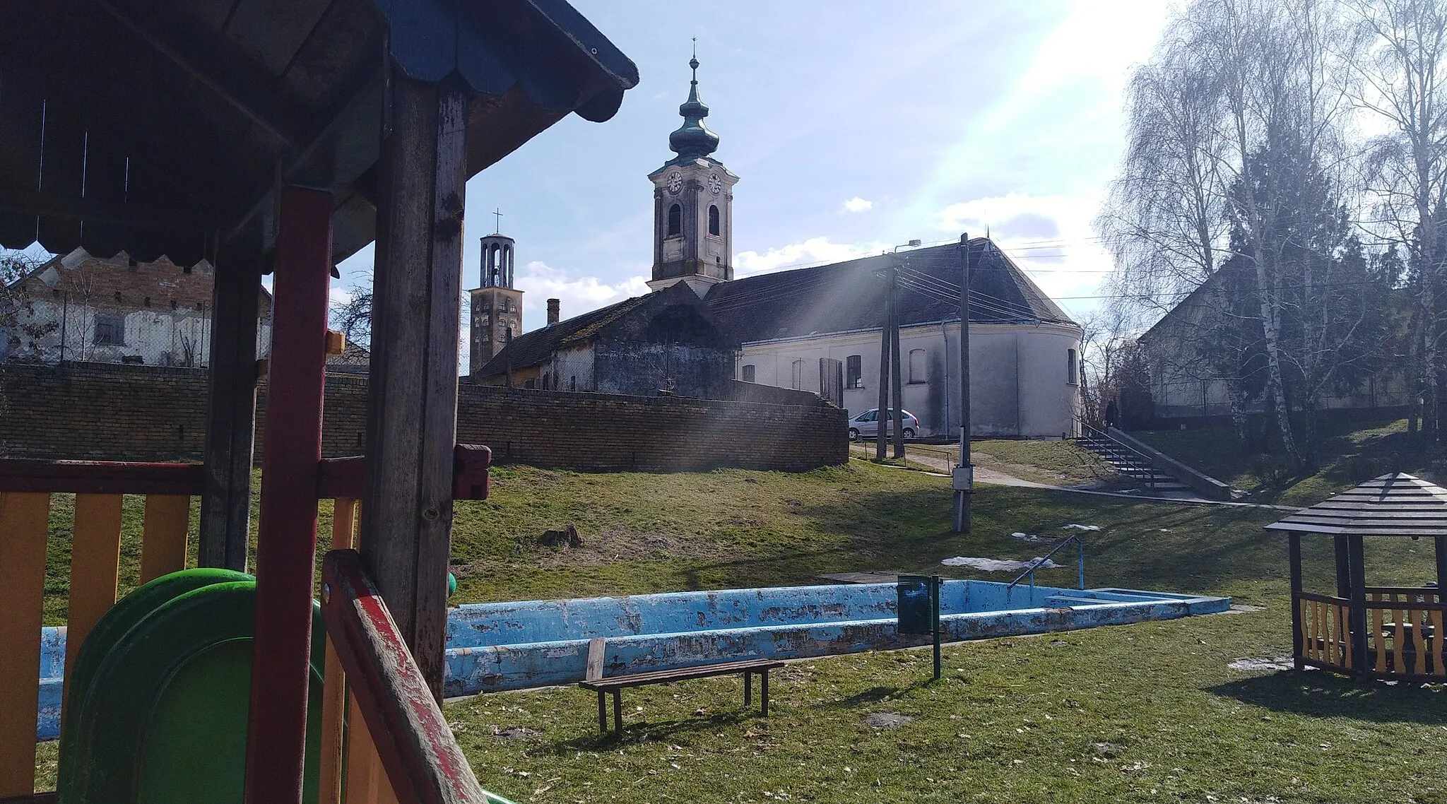 Photo showing: Reformed church (in front) and Roman Catholic church (at back) from playground in Őcsény, Tolna County, Hungary