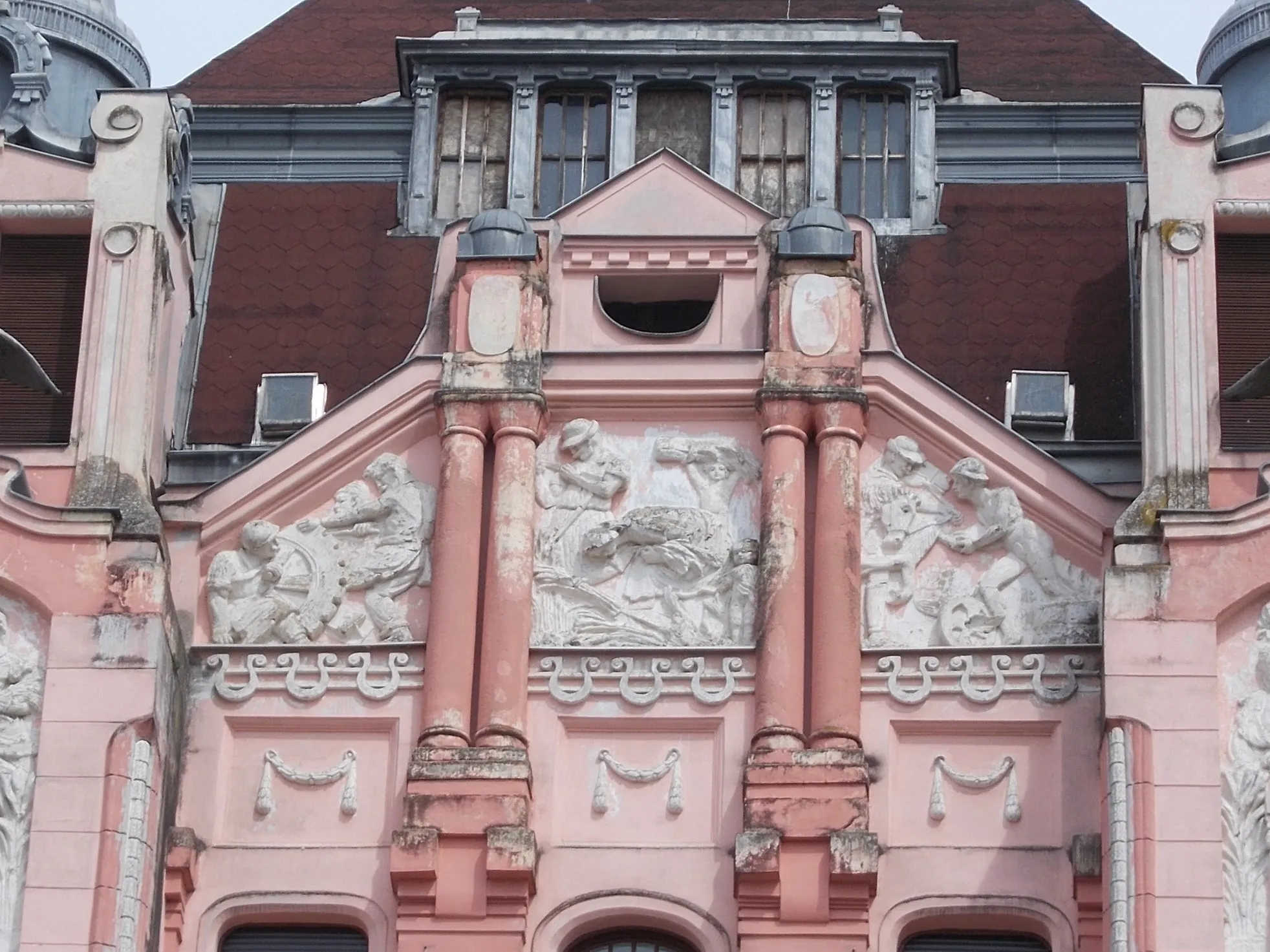 Photo showing: HQ of the former Debrecen First Savings Bank, west facade, mid part. Buil in 1912 Planned by Kálmán Rimanóczy Jr.. Construction contractors: István Tóth, Szilágyi and Pavlovits. Facade sculptures related to industry, agriculture and commerce and the nude male stuccos are Sándor Somogyi works ). There is couple bronze bird statues (Turul?). Inside coulmn capatáls made from Zsolnay ceramic. In addition to the premises of the Savings Bank, there were shops on the ground floor, on the Kossuth street side there were originally an officer's casino, in the cellar there was a beer hall and restaurant, on the floors there were seventeen luxury rental apartments. - 22-24 Piac Street, Inner City,Debrecen, Hajdú-Bihar County, Hungary.