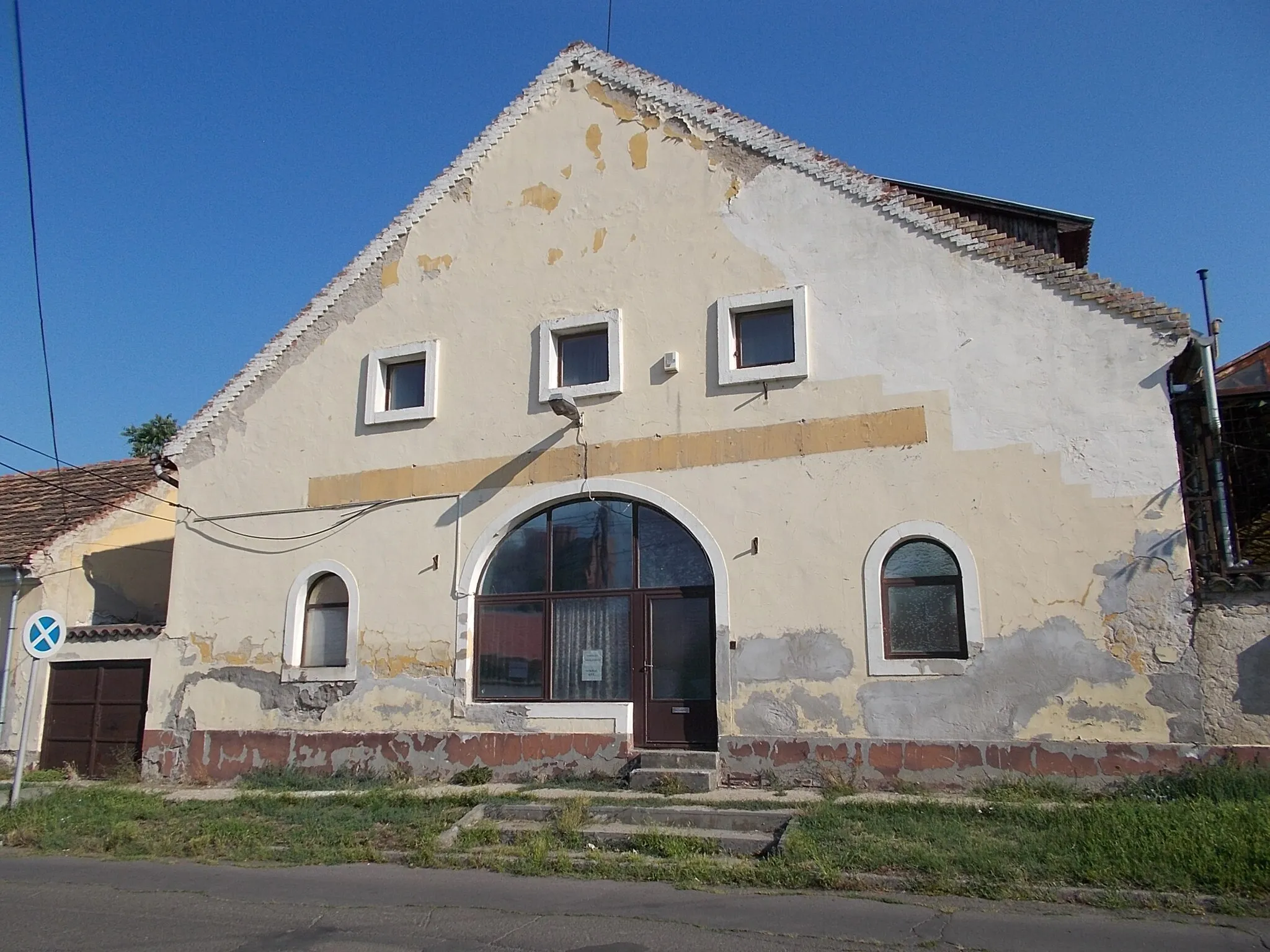 Photo showing: Angyal street's inn and farm buildings. Listed 5691 - Pesti road and Angyal street cnr., Gyöngyös, Heves County, Hungary - Angyal csárda és gazdasági épülete. Azonosító 5691. Három oldalról szabadon álló, földszintes, U alaprajzú épület, Ny-i főhomlokzatának középtengelyében nyíló kosáríves kapuval, a kapu zárókövén évszámmal (1757). A kapu két oldalán négy-négy vakolt, füles keretelésű ablak, a homlokzat két szélső tengelyében egy-egy egyenes záródású ajtó nyílik. Az oldalhomlokzatokon a Ny-i homlokzatéhoz hasonló ablakok.  Építtette Barkóczy Ferenc püspök (kivitelező: Berra Jakab építőmester).  1904-ben leégett, 1962-ben helyreállítva. Jelentések 2009-ből és 2014-ből Az épület csak pusztul és egyre rosszabb állapotban van. Az ott lakók nem törődnek semmivel. Az udvaron szemét és rendetlenség uralkodik.- Heves, Gyöngyös, Pesti út 2., Angyal utca 2.