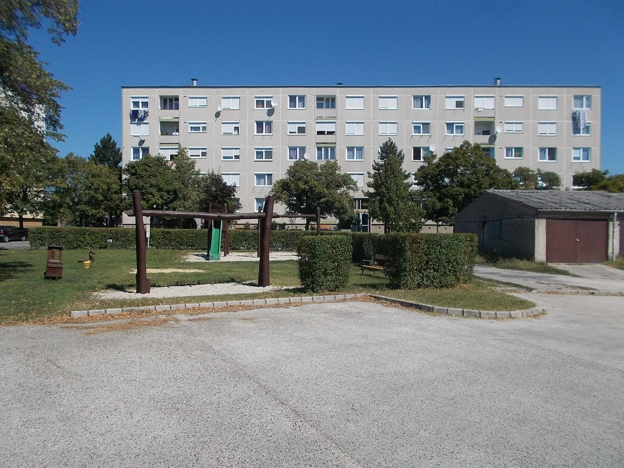 Photo showing: : Housing estate playground. Five floor Sümegi út Plattenbau apartment building (1960s, 1969?) and part of the garage line. - Sümegi út, West neighborough, Tapolca, Veszprém County, Hungary.