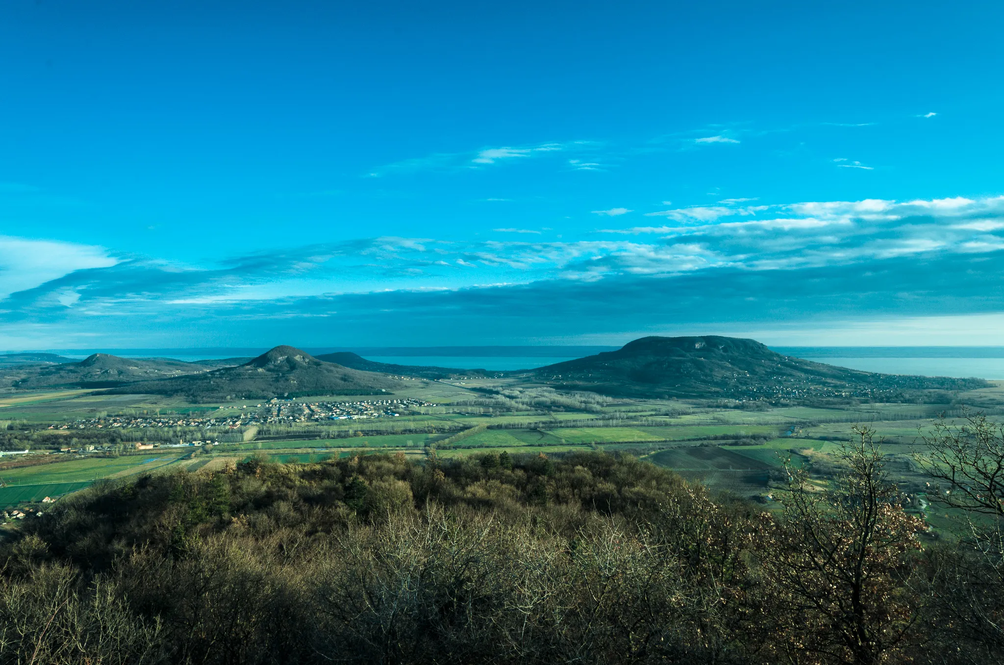 Photo showing: Some of the extinct volcanoes of the Bakony-Balaton Highland Volcanic Field near Lake Balaton in Hungary. The volcanoes are Tóti-hegy (on left), Gulács (in middle) and Badacsony (on right). These volcanoes are of Neogene age, between 3 and 6 million years old.
