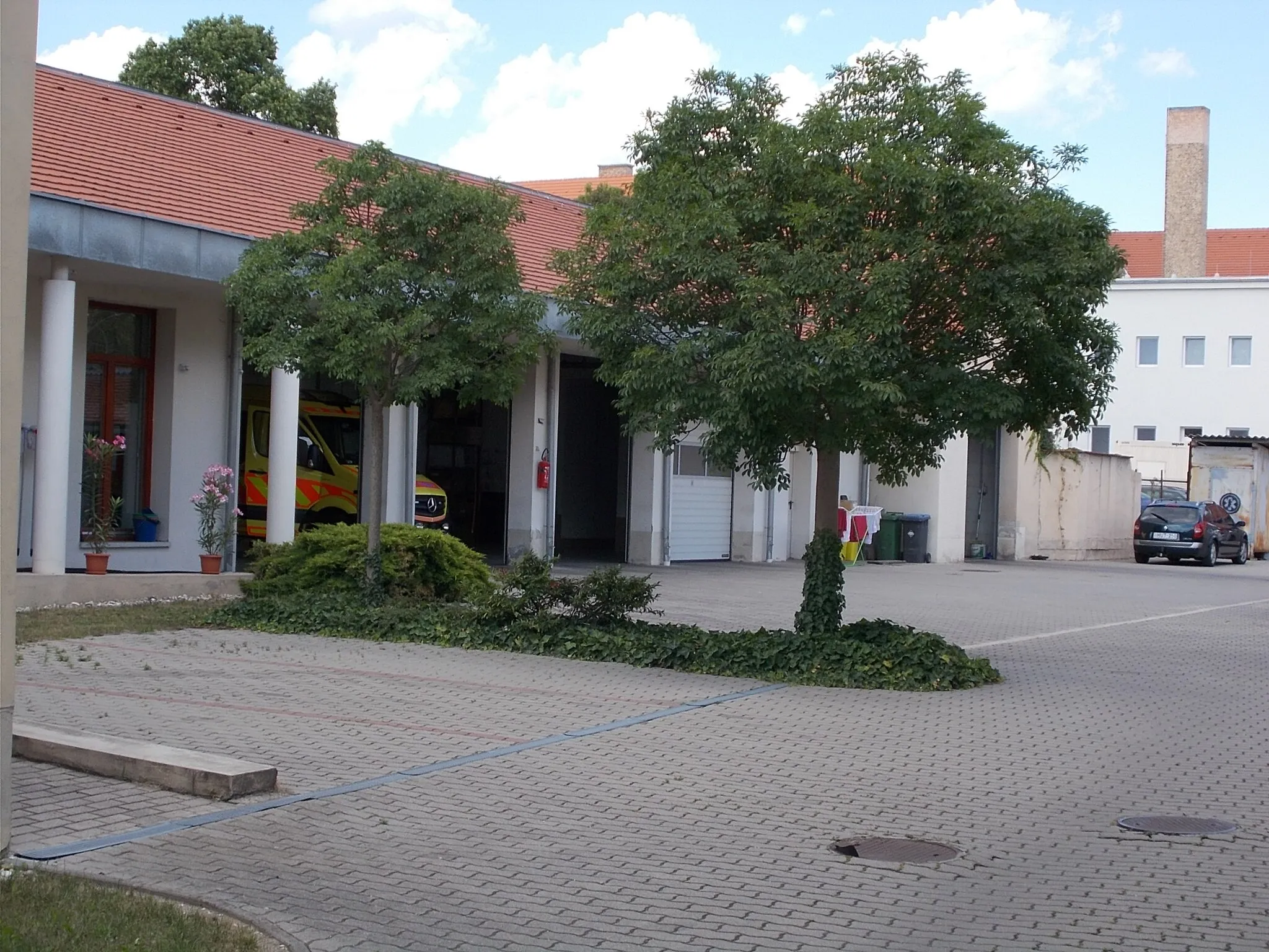 Photo showing: : Ambulance station, garages. Esterházy hospital chimney at back - 12 Anna Square, Downtown, Pápa, Veszprém County, Hungary.