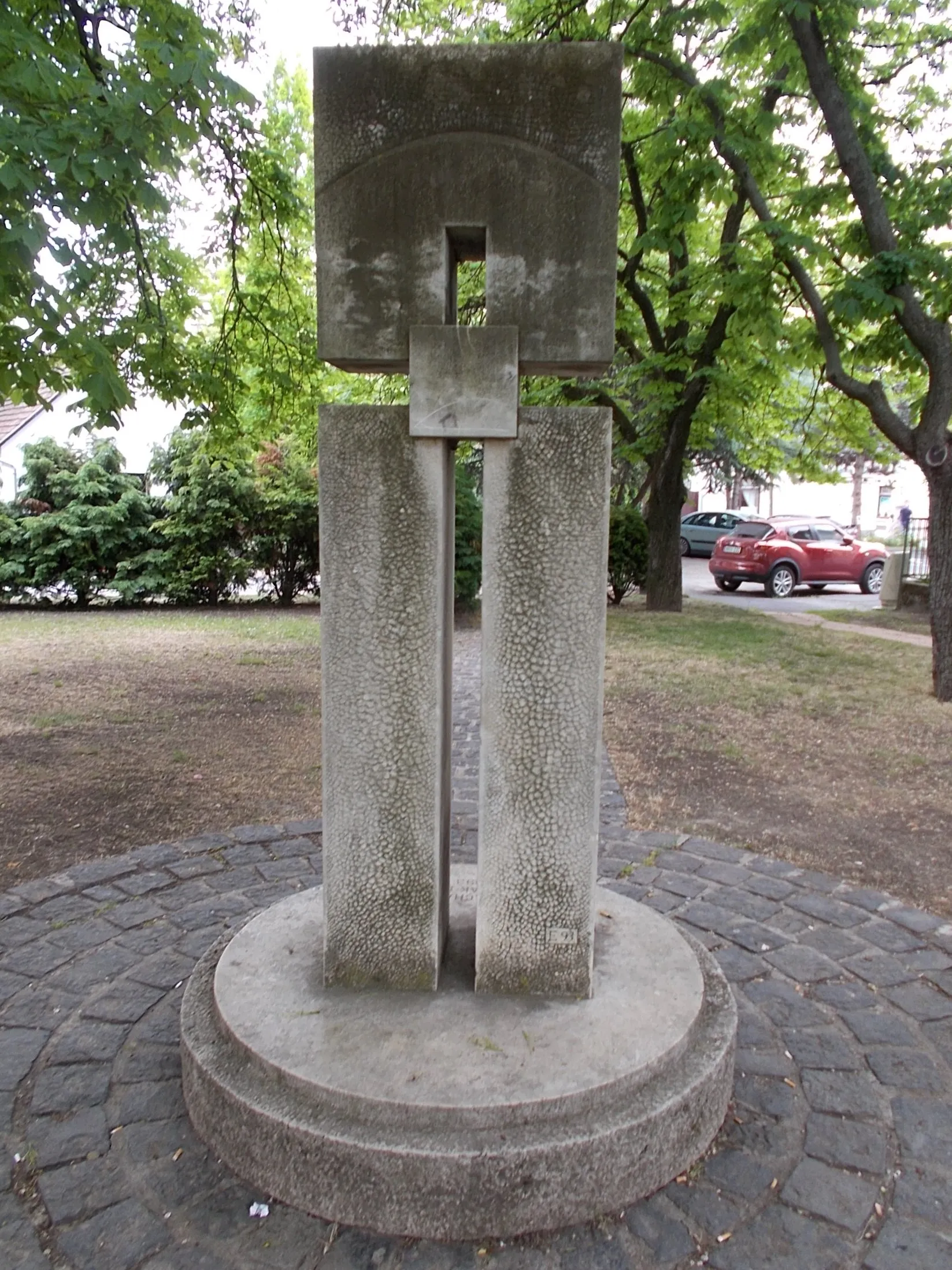 Photo showing: : World War II memorial by Emil Eőry (1993 limestone) in the church garden. From the sculptor:~overall, it is reminiscent of the totem pillars of natural peoples... quotes the Egyptian cult of the dead, but rooted in European Christian art. The geometric shapes create a negative cross, In the middle is the universal symbol a soul stone(?) that mean timelessness, immobility and connecting element of heaven and earth... - Szent István Square, Diósd, Pest County, Hungary.