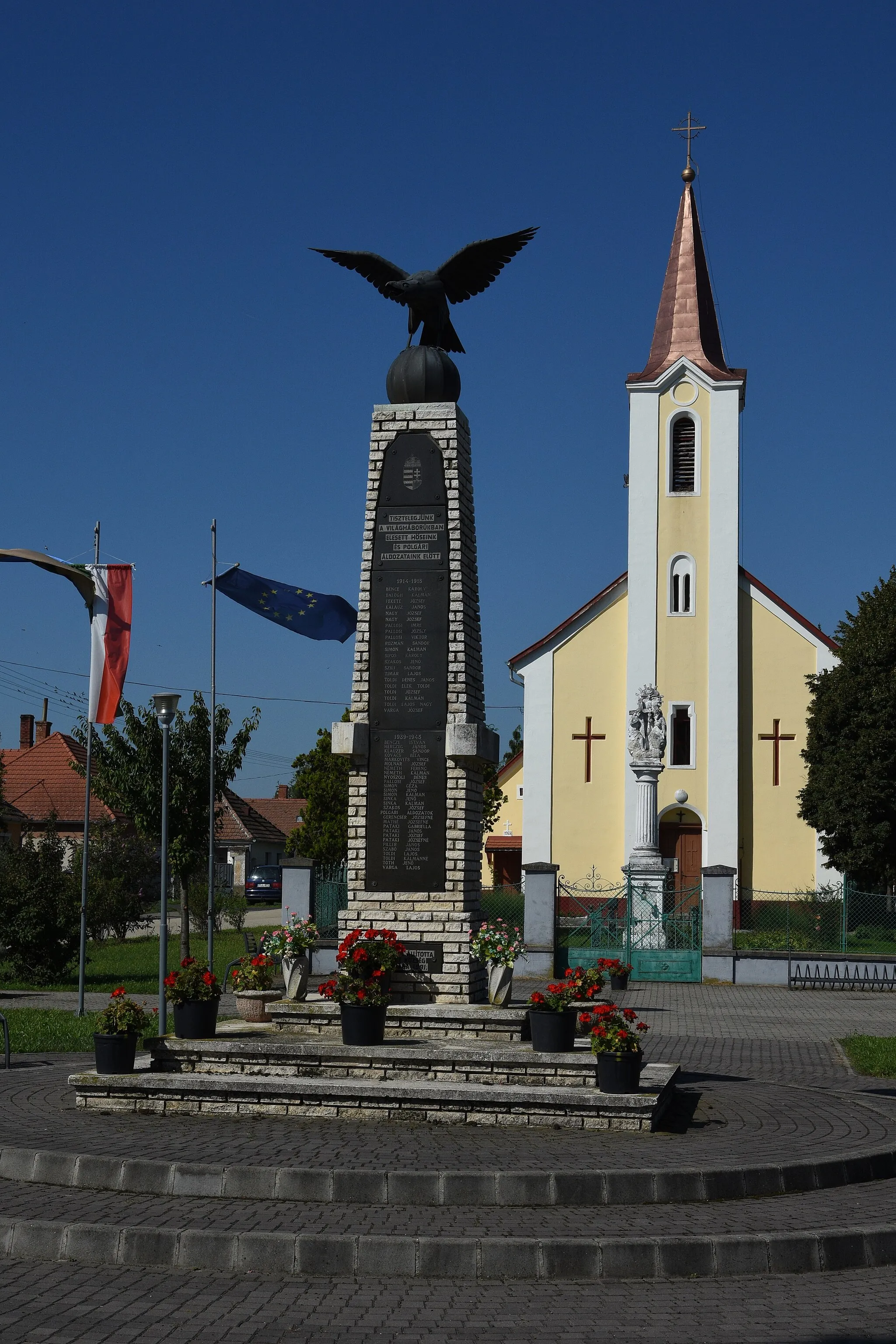 Photo showing: In front WWI and II memorial with turul statue (1991) at back Holy Trinity Church in Sótony, Hungary