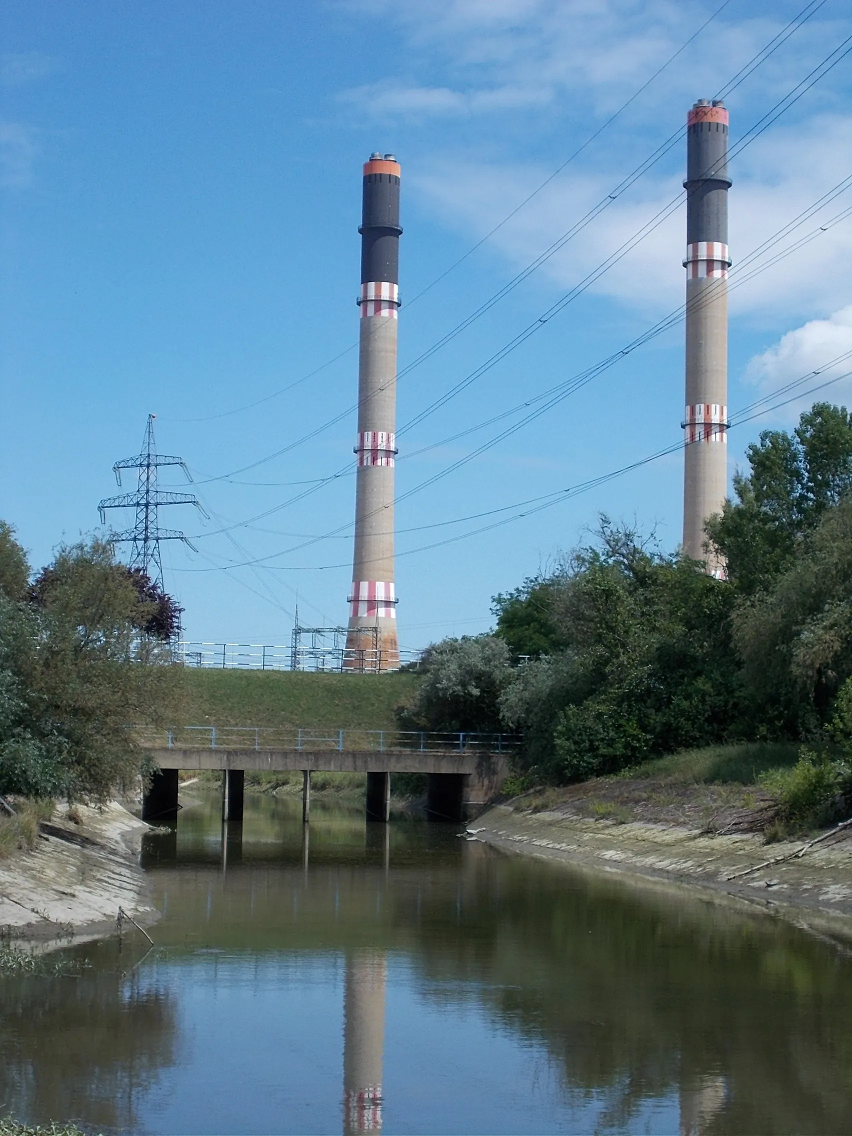 Photo showing: : In front a footbridge and behind its the Erőmű Road bridge over the Benta Stream, Power Plant two big chimneys, electricity pylon, overhead power line crossing,-partly,- the Stream - Százhalombatta, Pest County, Hungary.