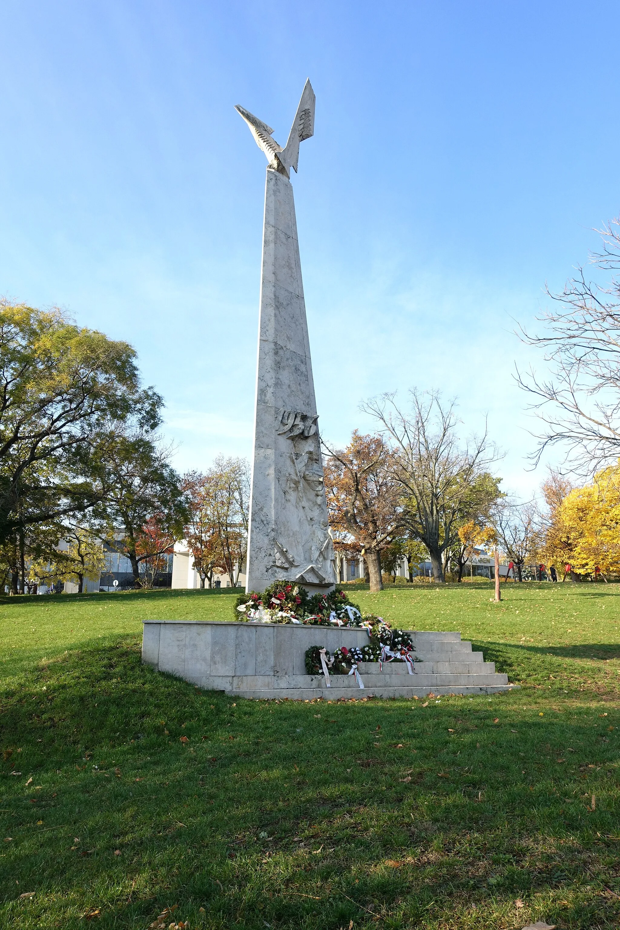 Photo showing: Memorial of the 1956 Revolution in Tabán Park, erected in 1996. Stone obelisk with a relief of freedom fighters and a stylized bird on top. Location: Tabán Park, Budapest District I., Hungary. Two plaques on the back-side: (1) Erected by a generous donation of the 1956 Hungarian freedom fighters living abroad, the 1956 Monuments and Piety Foundation, and Tibor Hornyák, József Vajda Németh and György Lassan freedom fighters. 1996; (2) This monument was erected for the 40th anniversary of our revolution by the Hungarian people and the surviving freedom fighters to the memory of the martyrs and participants in remembrance of the exemplary patriotism of the heroes / Those who sacrificed his life for the motherland has not died because the future generations of posterity will remember the glorious memory of the heroes of 1956 / Board of Trustees of the 1956 Monuments and Piety Foundation