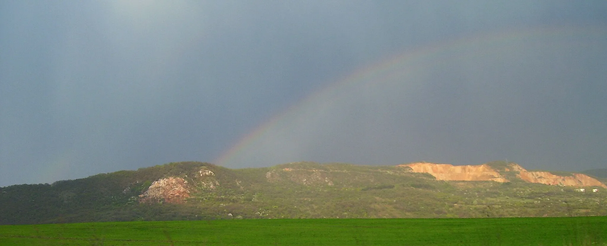 Photo showing: Photo of the Naszály mountain (in northern Hungary, 652 m) taken from southwest. Lime-pits of a cement plant and a rainbow can be seen on the picture.