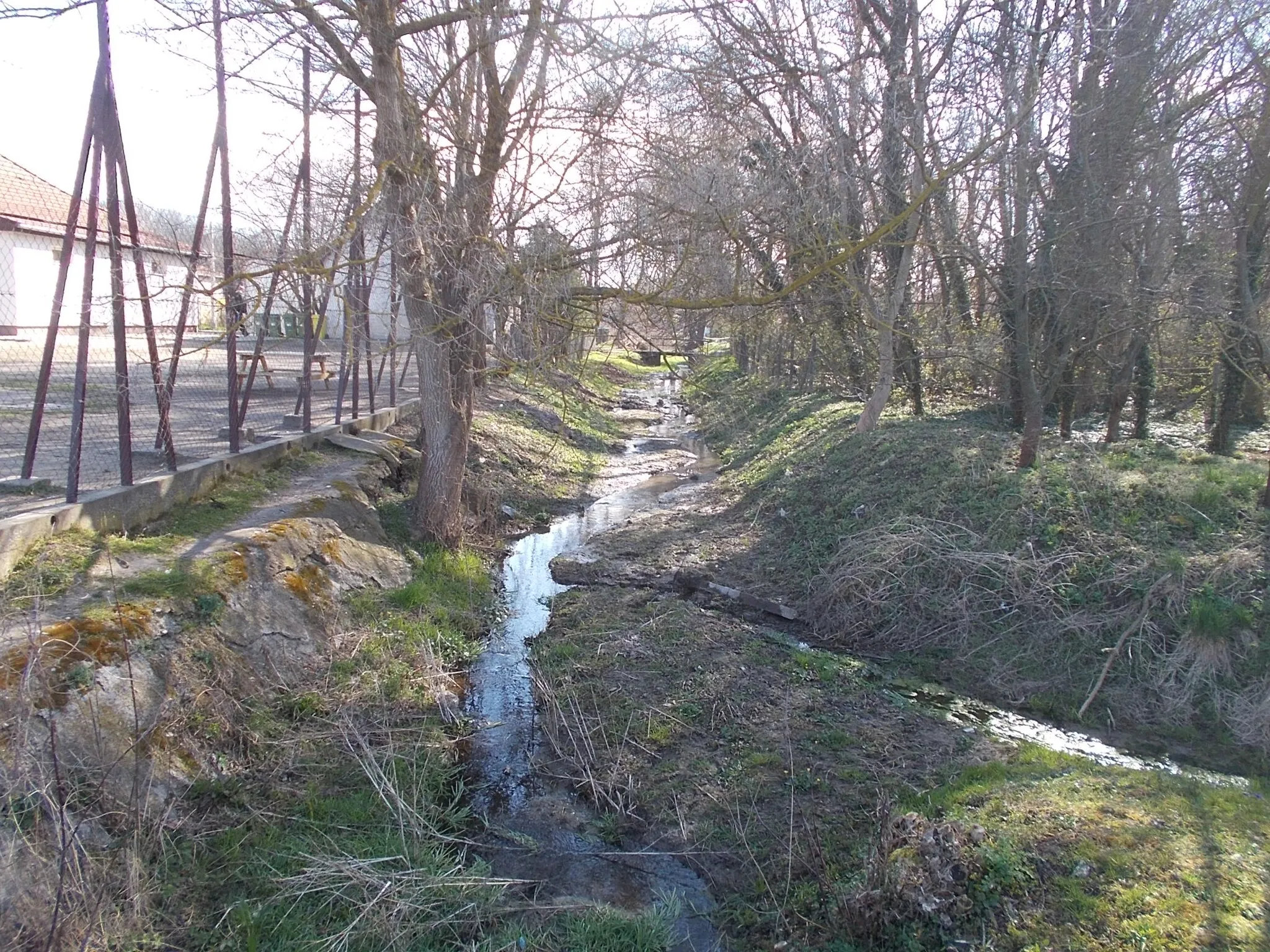 Photo showing: View from Iskola 'ulicska' current/footbridge over Bénye Stream. 1953 work. Bénye Stream cleaned (recreated?) in 1959. There were once 21 springs in the settlement. Most of them in the 21st century no longer work, do not provide water - Bénye, Pest County, Hungary.