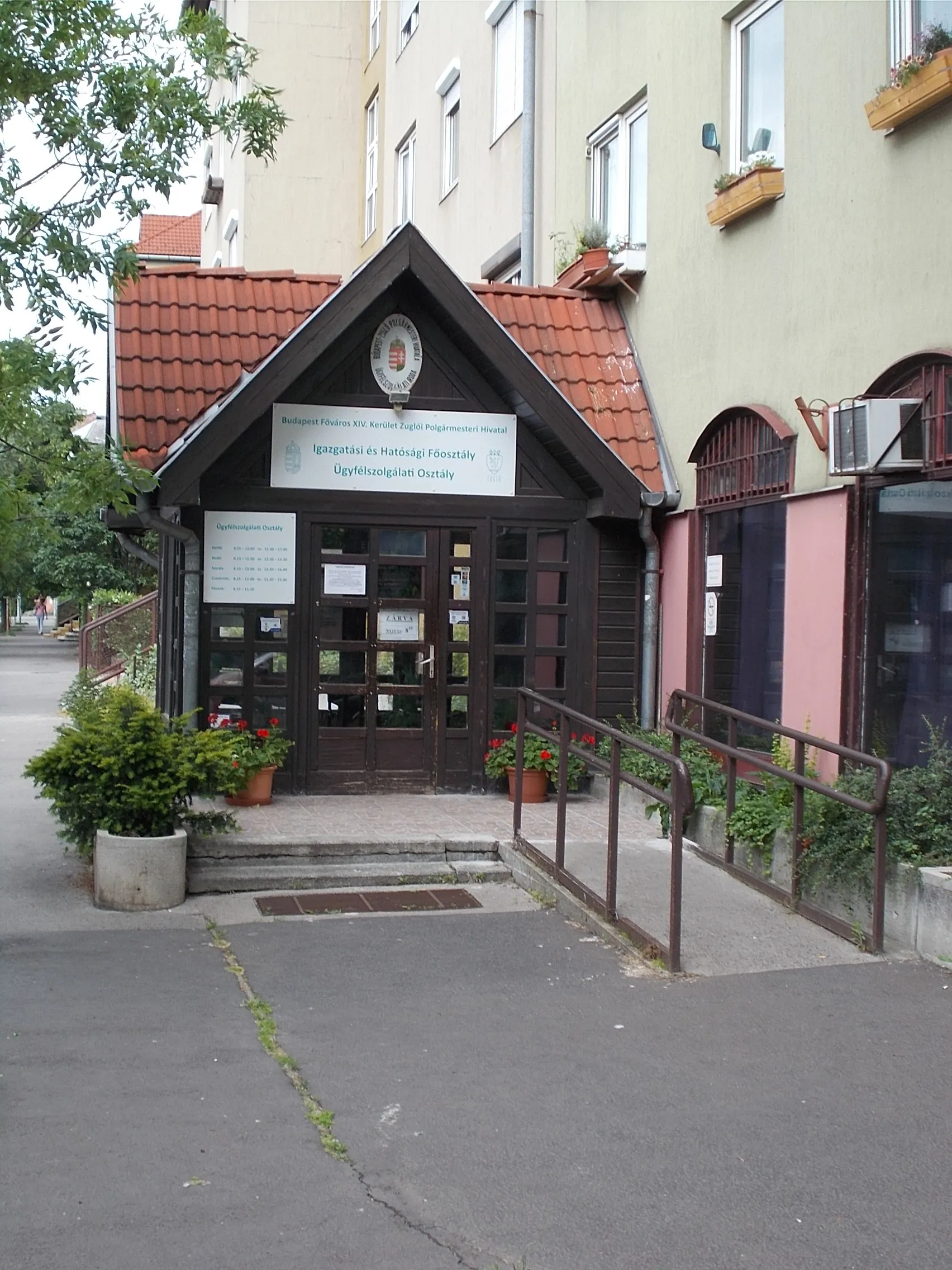 Photo showing: Four-story corner residential building with a four-storey, closed balcony. On the ground floor (in 2023) is ~'Customer Service of the Administration and Authority Department of the Budapest Capital XIV. district Zugló Mayor's Office' - 11 Nagybecskerek Street= 53 Bácskai Street, Herminamező neighborhood, 14th district of Budapest.