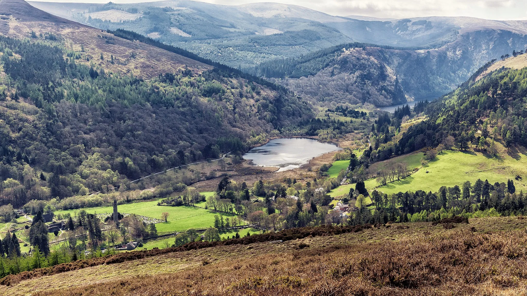 Photo showing: Photograph of the Glendalough Valley, County Wicklow, Ireland, facing south-west, taken from the south-east slope of Brockagh Mountain, showing the early Christian monastic settlement, the Lower Lake and the Upper Lake that give Glendalough ("The Valley of the Two Lakes") its name, flanked to the south by Derrybawn Mountain and Lugduff Spink and to the north by Camaderry Mountain.