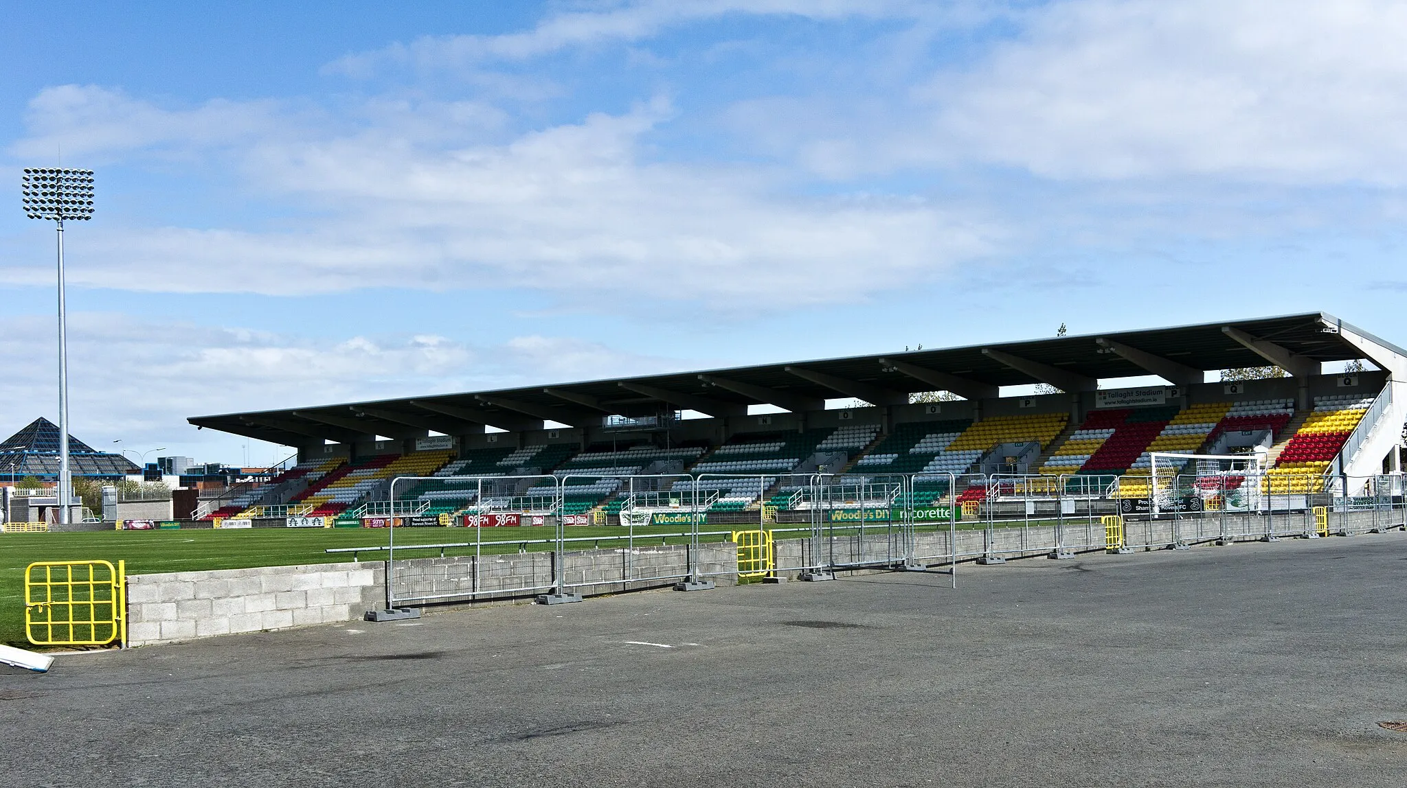 Photo showing: Tallaght Stadium is a football stadium in the Southside suburb of Tallaght. Shamrock Rovers originally announced details of the stadium back in July 1996.
The stadium is owned and operated by South Dublin County Council with Shamrock Rovers as the anchor tenants.
The main stand seats 3,048 and holds home supporters, away supporters, club officials and press. A second stand seating 2,899 on the opposite (east) side of the ground, was completed in August 2009. This stand holds the stadium's TV gantry and has brought the seating capacity to 5,947. Both stands are covered. There are no stands currently in place behind the goals. Refreshment stalls are located at the southern end as is a stadium control room.
Temporary seating has twice been constructed at the stadium. Once for a club friendly against Real Madrid which gave the ground a temporary capacity of 10,900 and again before the 2009 FAI Cup Final, giving the ground a temporary capacity of 8,800.

Located behind the main stand is the Shamrock Rovers club shop jointly operated by Rovers and kit suppliers Umbro. Also onsite at the stadium is the 'Glenmalure Suite' open to club members on match days.