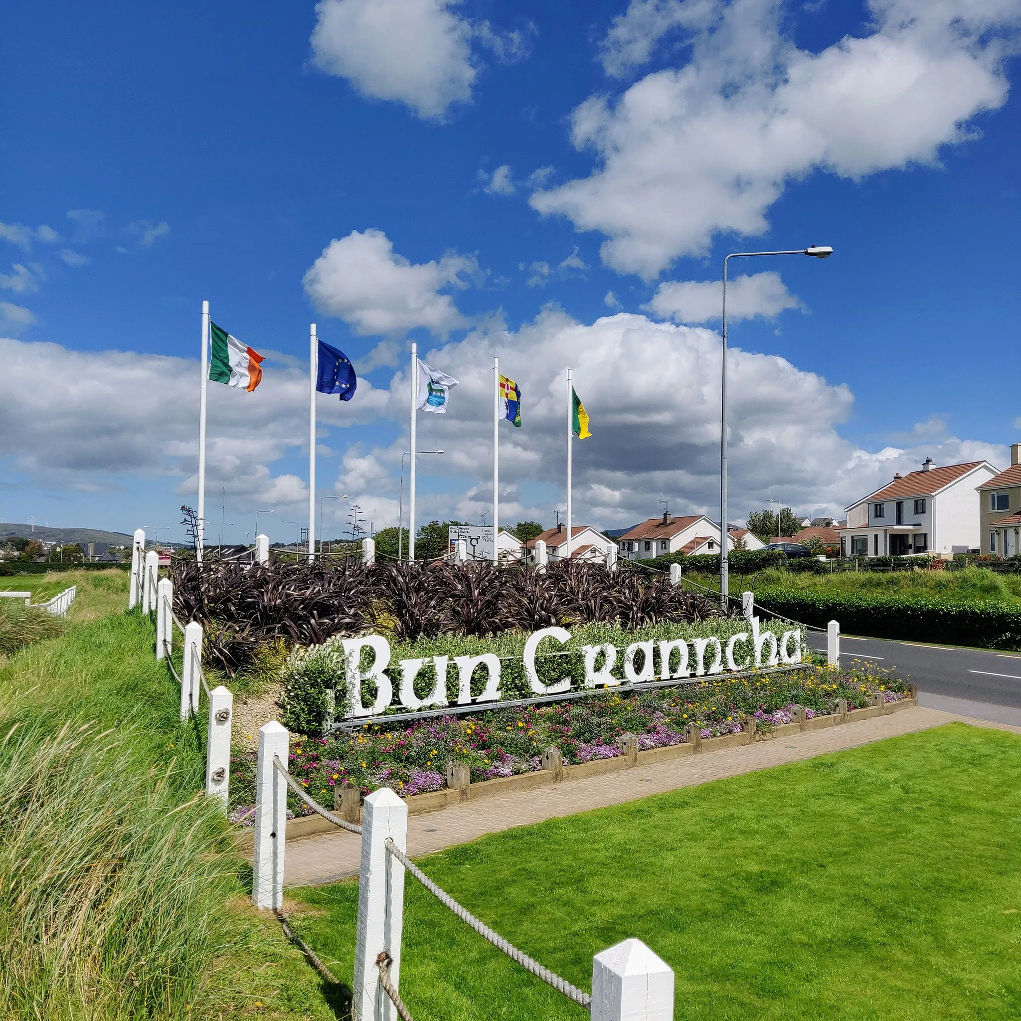 Photo showing: Bun Cranncha displaying various flags, as seen when entering via Railway Road R238