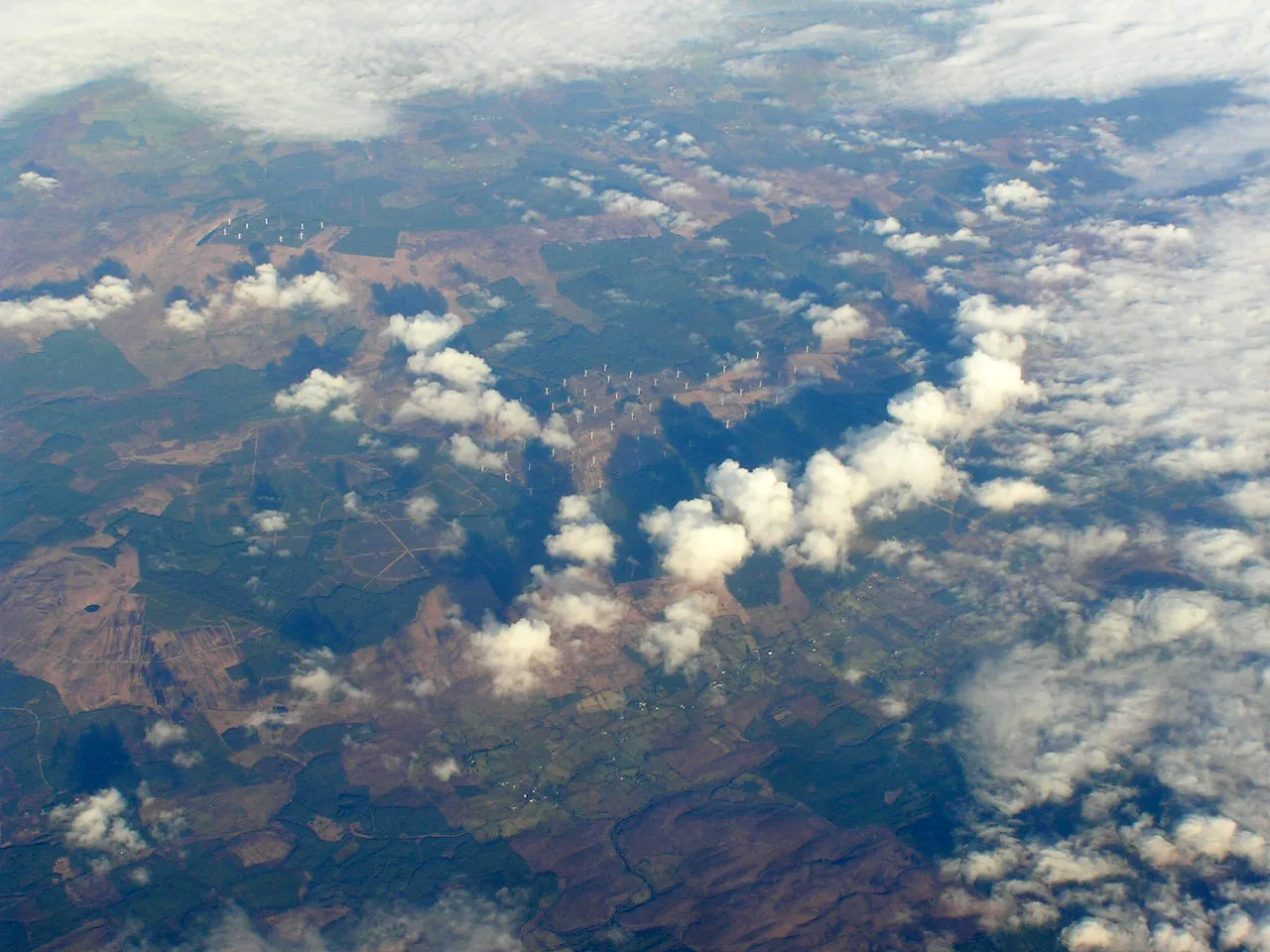 Photo showing: Another wind farm, this one built above the village of Derrybrien (running just below that line of clouds) and also called Derrybrien. It's the largest wind farm in Ireland. The hill it's built on has the awesome name of Cashlaundrumlahan.

The almost perfectly round hole in the lower left is a lake called Divney's Lough. I wish I knew more about it; like: why is it almost perfectly round?