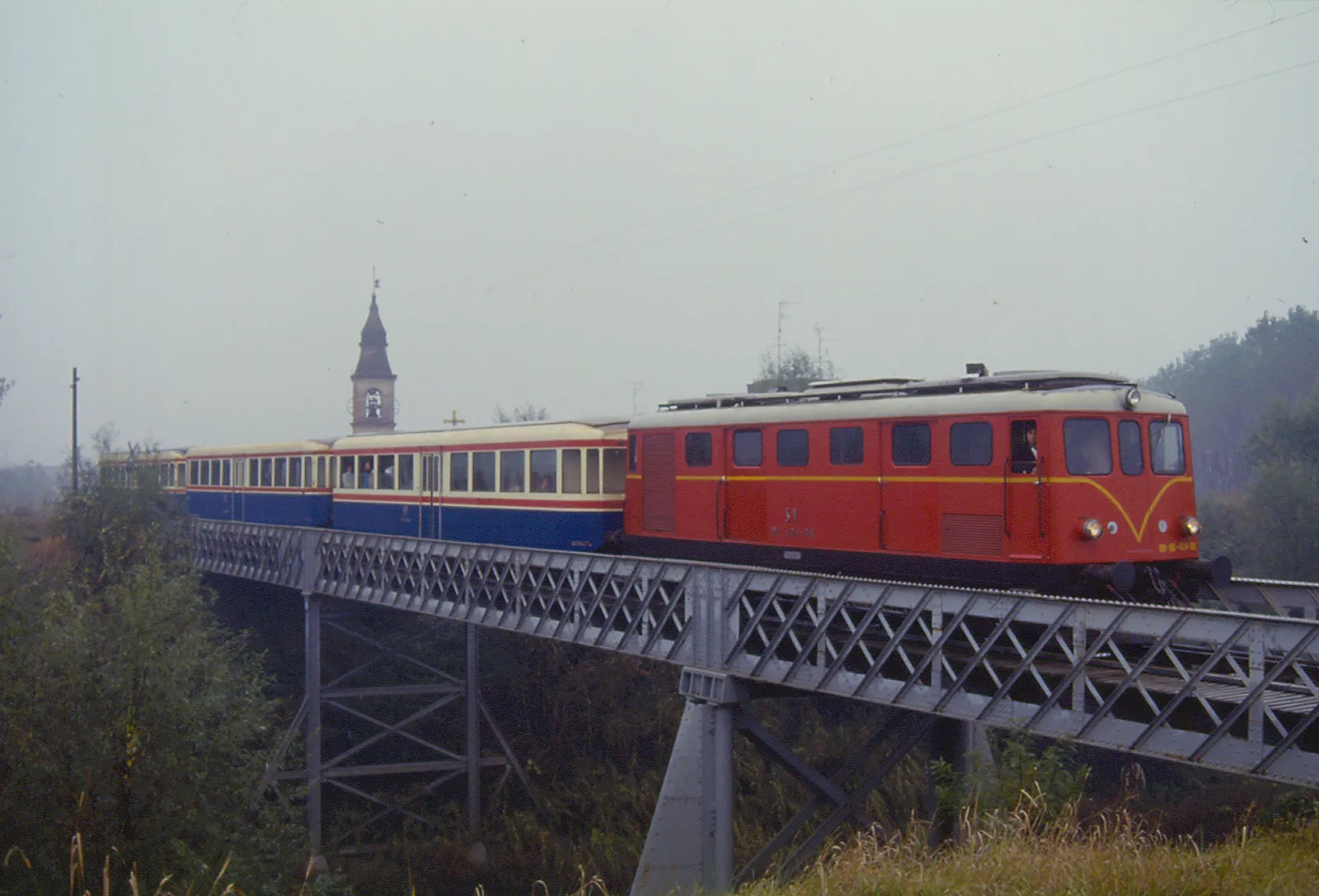 Photo showing: Il locomotore DE.424.08, nella sua sgargiante livrea storica, di SV (Società Veneta per le imprese e costruzioni pubbliche) è qui ripreso il 19.10.1986 sul ponte sul torrente Crostolo mentre traina un treno speciale in occasione dell'assemblea annuale A.F.I..
La linea Parma-Suzzara qui impegnata (44 km. di lunghezza, inaugurata nel 1883) è confluita nel 2001 nell'attuale società Ferrovie Emilia Romagna.