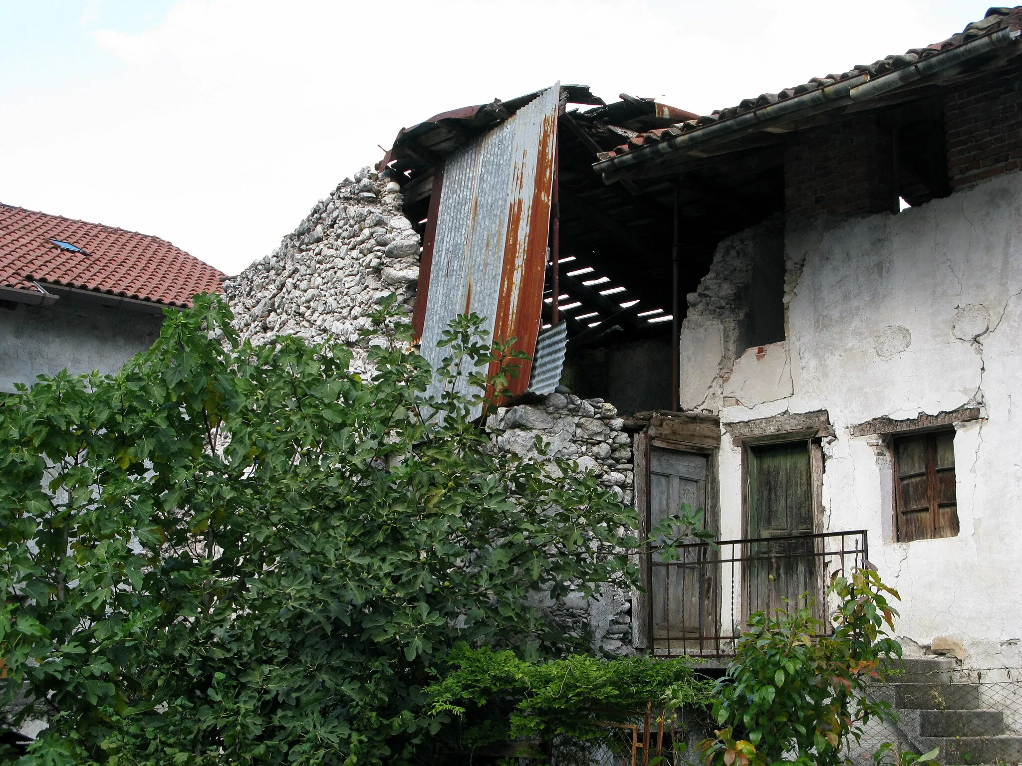 Photo showing: Rotten house in the middle of San Giorgio in Resia valley, a tributary valley of Canal del Ferro / Friuli-Venezia Giulia / Italy / EU. Wall collapsed in part is protected by a makeshift corrugated iron. In front of the house is a fig tree.