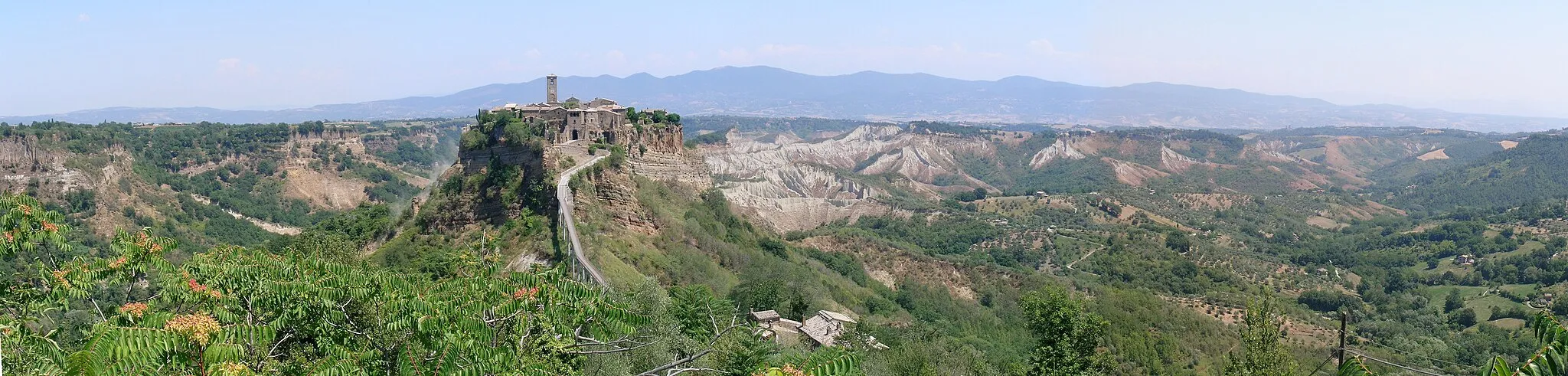 Photo showing: Bagnoregio is a small town in Lazio, Italy. The old part, called "civita", is on the top of the hill. This picture shows the "civita" and the surroundings, under a strong summertime sun, it's a panorama made of 3 pictures stitched together