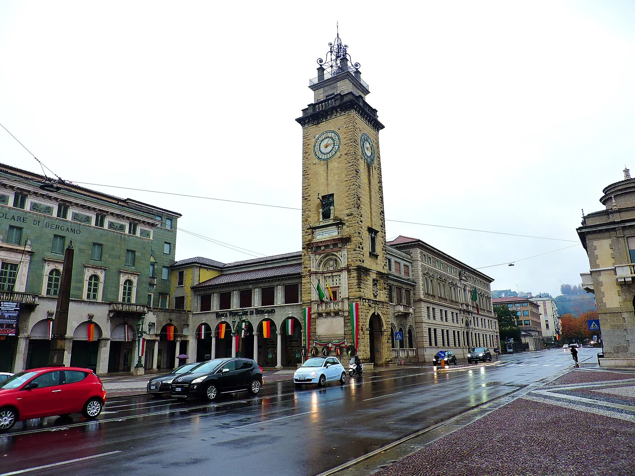 Photo showing: This monument was erected in remembrance of the sacrifice of numerous young men fallen during the First World War. At the same time, it also represents the centre of the new and modern Bergamo, the one that was created in the early XX Century outside the walls, featuring wide and open spaces.
The square below is used to host the most significant official ceremonies, such as the celebration for the Republic Day, on June 2nd, or the Guardia di Finanza Cadets Oath. The Memorial Tower (“Torre dei Caduti” in Italian) stands in a central place for Bergamo citizens: if you visit the city during weekends or holidays, you are likely to see the square and the streets filled with market stalls, displaying local products, candies and handicrafts.
Also several Fairs take place here, such as the Book Fair or the most anticipated event in October, the Fair gathering merchants from all over the world.
The famous speech held by the General Diaz, leader of the Italian army announcing the victory and the end of the First World War, demonstrates the original use of the Tower as a symbol of collective memory.
The marble statues of the façade refer to the Roman history and inspire a sense of sacredness. Going up inside, instead, the atmosphere is more intimate and contemplative. The names of the many young men from Bergamo died during the War are written in gold over the black walls.

Source: www.visitbergamo.net