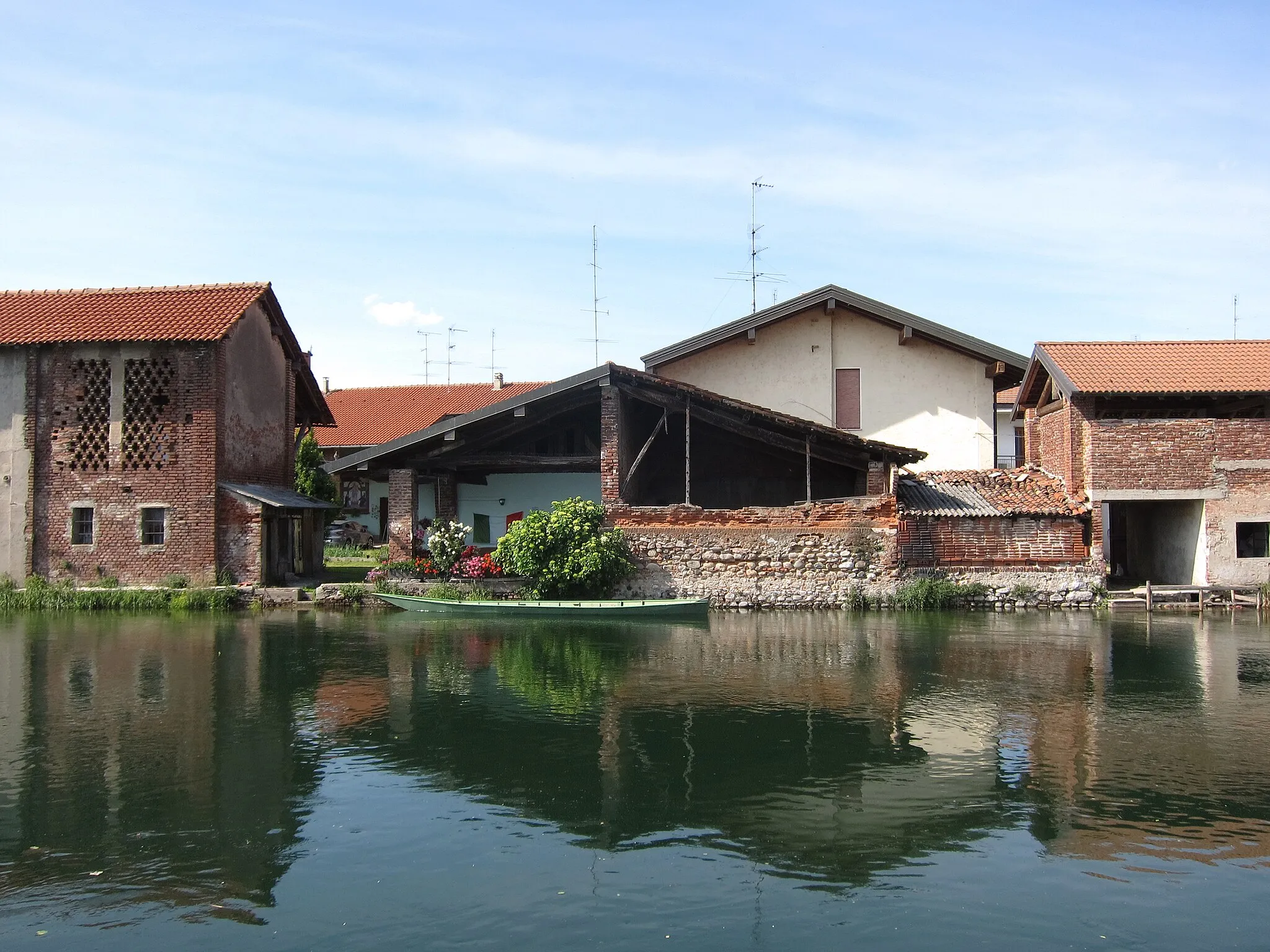 Photo showing: Old bricks buildings and a docked row boat on the coast of the canal Naviglio Grande. This place is located in the municipality of Bernate Ticino in the Province of Milan in Lombardy in Italy. Picture taken on the 24th of May 2020.   2020-05-24