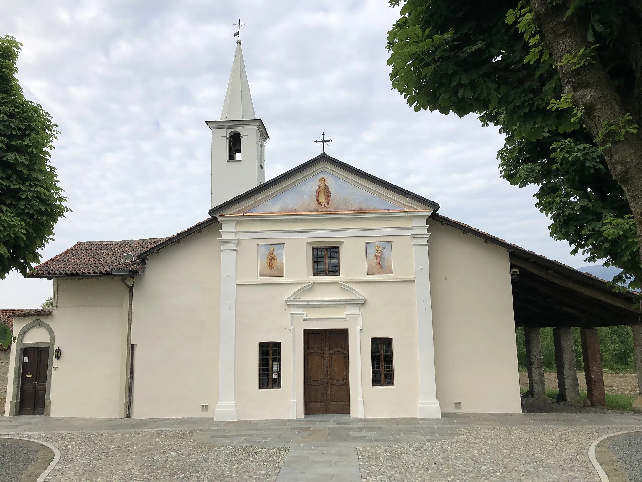 Photo showing: Affonda le radici nel passato più remoto la devozione dei nolesi al martire Vito: già agli inizi della storia del paese si ipotizza l’esistenza di un luogo dedicato al santo, di cui è rimasto nel XVI secolo un pilone votivo con l’effigie del santo dipinta. Il luogo si trovava sulla strada che dal torrente Stura portava, e conduce tuttora, al centro abitato di Nole; per questo motivo era un tratto molto frequentato e i nolesi erano particolarmente legati a quell’edicola votiva. Passando accanto all’immagine, infatti, raccontano i prevosti nelle cronache parrocchiali, non mancava mai una sosta e una preghiera al santo, spesso con una richiesta di grazia che veniva concessa dal Signore, per l’intercessione di san Vito.
Cronistoria
Metà XVI secolo: presso la strada che conduce dal torrente Stura al centro di Nole sussiste il pilone votivo con l’immagine del santo.
Fine XVI – inizio XVII sec.: la comunità nolese, per la grande devozione degli abitanti e dei passanti, inizia a costruire una piccola cappella attorno all’edicola votiva. Probabilmente a questo periodo risalgono i due affreschi che si possono vedere ai lati dell’altare, raffiguranti sant’Antonio Abate e san Giovanni Evangelista.
Metà XVII sec: la prima chiesa è decorata con gli affreschi della volta: una finta architettura che spalanca la volta del santuario verso il cielo, al centro probabilmente l’immagine di san Vito nella gloria, ora perduta. Già dal Seicento esistevano, accanto alla chiesa, due stanze per l’abitazione del romito (armit nella parlata nolese), che da tempo immemorabile è posto dalla comunità a custodia del santuario, essendo al di fuori dal paese.
1648: viene ridipinto l’affresco del pilone centrale che assume l’aspetto odierno: il pittore locale Lorenzo Lega riproduce il giovane martire san Vito al centro, con accanto i due santi Pietro e Giacomo Apostoli, in alto Gesù Cristo e la vergine Maria che incoronano il santo porgendogli la croce e la palma del martirio.
Prima metà XVIII sec.: il primo ampliamento della chiesa prevede la costruzione della navata centrale e successivamente le due cappelle laterali con gli altari dedicati alla Madonna d’Oropa e a san Vincenzo Ferrer, quest’ultimo successivamente intitolato a san Giuseppe e ora altare devozionale di san Vito. Vengono quindi decorate le pareti e le volte della navata e delle cappelle laterali.
Nel 1794 a seguito di una grazia ottenuta dal santo martire Vito, si ritira in eremitaggio presso il santuario il conte Amedeo Cavalleri di Rivarossa: ferito in battaglia sulle Alpi Marittime, il 14 giugno 1794, fu salvato per l’intercessione di San Vito. Giunto presso il santuario vi abitò fino alla morte, nel 1837, e apportò numerose modifiche alla struttura della casa attigua, ampliando i locali e realizzando il giardino adiacente, con il muro di recinzione che termina con un’esedra dove il conte ha fatto rappresentare su affresco il motivo della sua presenza, cioè il ferimento nella battaglia. Dal momento del suo ritiro a San Vito iniziò per il Conte una nuova vita: spese le sue giornate nella preghiera e nella solitudine del santuario, offrendo accoglienza ai pellegrini e una testimonianza cristiana vera.
Sec. XIX: il santuario assume l’aspetto odierno con l’aggiunta della galleria degli ex voto (prima i quadri erano conservati direttamente in presbiterio, appesi sulla parete di fondo affrescata) e dell’attuale sacristia nella zona retrostante l’affresco originario.
1992: si provvede al rifacimento della pavimentazione interna della chiesa, sostituendo le piastrelle con la pietra attuale.
1998: viene rifatta la copertura del santuario.
2002: si inaugura la stagione dei restauri interni: vengono riscoperti e riportati all’antico splendore settecentesco prima gli affreschi dell’altar maggiore, con il retablo ligneo, poi le decorazioni parietali e della volta della navata centrale e degli altari laterali, concludendo nel 2012 con la volta seicentesca dell’attuale presbiterio.
2013: si completa il restauro dell’interno del santuario con la risistemazione della galleria degli ex voto: adeguamento della decorazione muraria, nuovo sistema di esposizione dei quadri, rifacimento dell’impianto di illuminazione.
2017: la collaborazione con il Comune di Nole permette la risistemazione del sagrato del santuario, con la nuova pavimentazione in pietra e ciottoli; la pedonalizzazione dell’area la rende più fruibile al pubblico e conserva la sacralità del luogo.

2018: nei mesi di marzo e aprile, viene realizzato il restauro della facciata del santuario, con il rinforzo dell’intonaco, la tinteggiatura e il restauro dei dipinti (raffiguranti san Vito, nel timpano, san Modesto e santa Crescenzia, nelle due nicchie in basso), già restaurati e in parte integrati nel 1960 dal pittore Vincenzo Sebastiano da Levone.