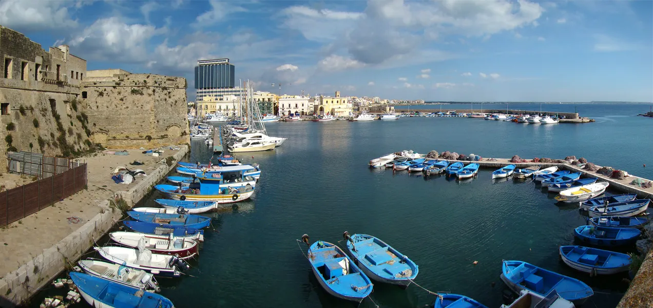 Photo showing: Gallipoli, Apulia, Italy. The south harbour seen from the old town. In the foreground on the left, the walls of the Angevine-Aragonese Castle. In the background, the new town on the other side of the bridge.