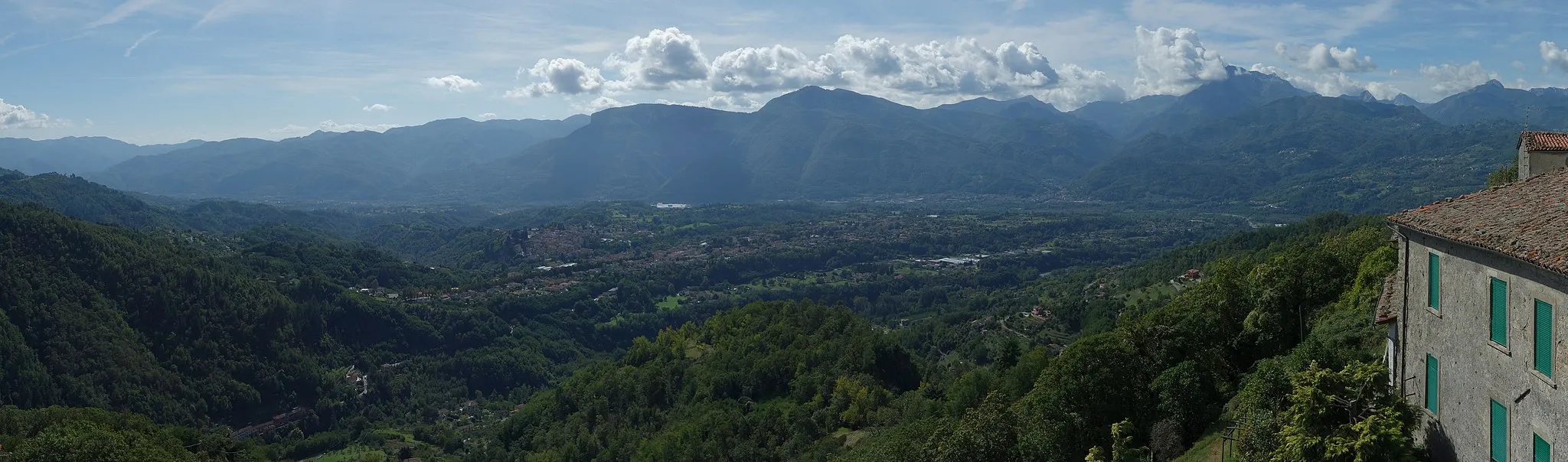 Photo showing: A panorama taken from Sommocolonia, a small hillside village which belongs to the town of Barga in the region of Garfagnana, Tuscany, Italy. The image shows the valley of the Serchio river with the Apuan Alps in the background. In the center Barga can be seen and at the feet of the Apuan Alps one can make out Gallicano. The tallest visible mountain, at the right, its summit partly obscured by clouds, is Pania Secca.