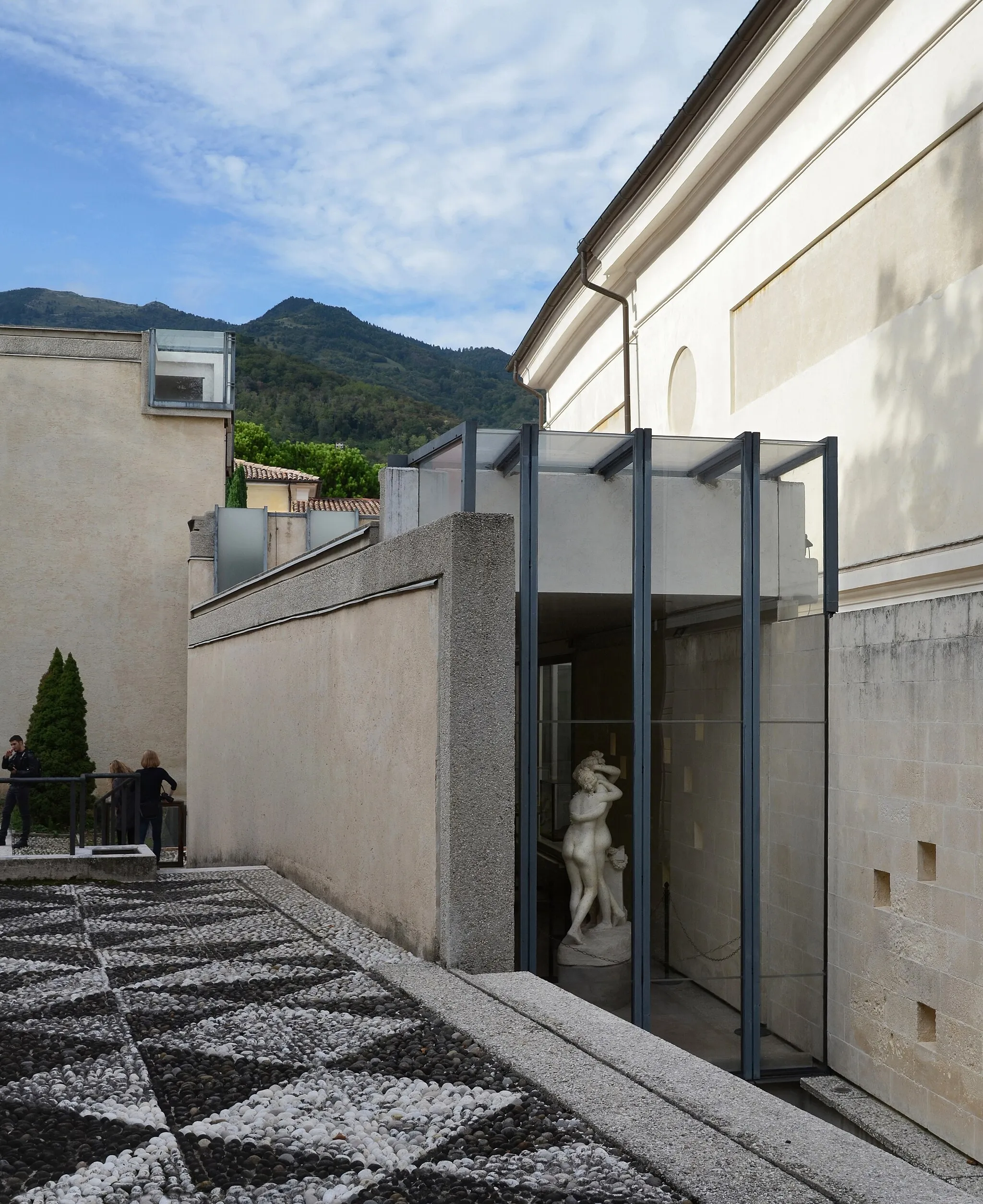 Photo showing: gipsoteca del canova, canova plaster cast gallery extension, possagno 1955-57.
architect: carlo scarpa 1906-1978 with v. pastor.
view from the south.
to the right is the original, 19th century museum. the rooms of scarpa's extension are articulated almost as individual buildings and follow the the outline of earlier houses on the site, giving us an example of the layered compositions he would later be famous for.
even if this layering is less extreme than in scarpa's final buildings, the elements of his architecture are carefully drawn apart and given their individuality before being assembled. the windows are the obvious example here, most are highly original takes on the modernist corner window, physically lifted out of the walls they would normally be set in. I count five distinctly different light sources in this photo alone - and remember that the interior is one continuous, unfolding space.
but we should also look at the walls. right to left, we find three walls that are not quite parallel, not of the same height, and not built in the same way. the first one is the imposing outer wall of the first museum. its detailing and decoration is entirely conventional, but it gains its presence from sheer size.
the second wall, at a distance from the old museum, delineates the new building but does little else. it does not support anything other than itself (the roof being supported on a steel beam). yet it gains an expression of equal intensity to its much larger neighbour by being in natural stone, almost as if it were a found wall.
at an angle and at a different height is finally the main wall of scarpa's extension, separated into a concrete frame and a rendered, blank wall. I believe scarpa is creating a syntactical relationship between the separated parts which is as strong, albeit very different from, similar walls united in a traditional box. we often talk about this, especially in the later works, using words like fragments or fragmentation, but there are negative connotations to words like these that are not true of the architecture they are meant to represent.
(the steel mullions in the window facing the three graces are not original, if I remember correctly. I think they were hardwood when I saw them first some twenty years ago).
this photo was uploaded with a CC license and may be used free of charge and in any way you see fit.
if possible, please name photographer "SEIER+SEIER". 
if not, don't.
do NOT copy texts, tags and comments.

the scarpa set.