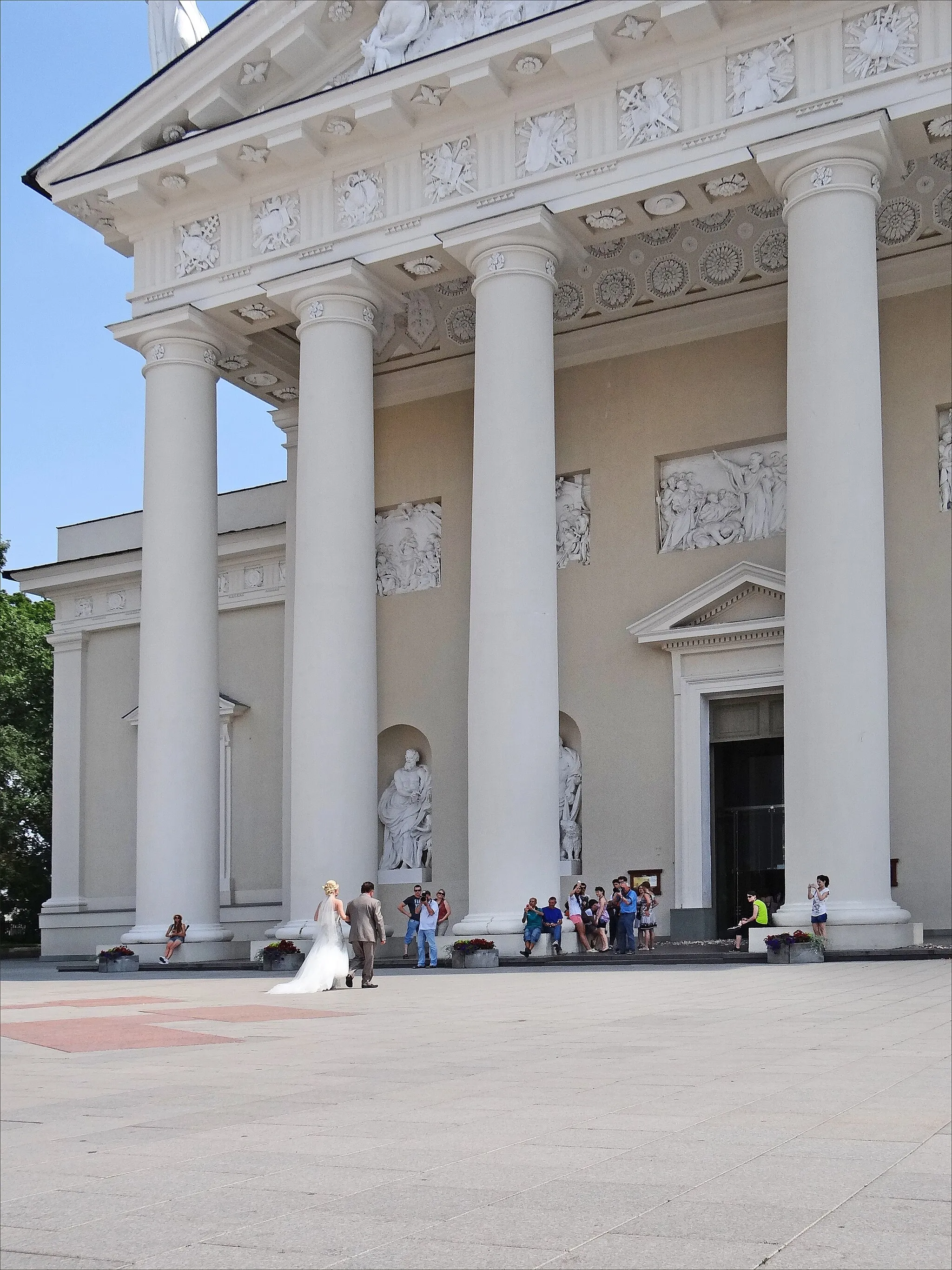 Photo showing: Devant la cathédrale de Vilnius, une mariée au bras de son père.
_____

La fête du couronnement du roi Mindaugas, fondateur de l’État lituanien est le 6 juillet, un vendredi en 2012, ce qui a permis aux lituaniens de bénéficier d'un long week-end. Beaucoup en ont profité pour se marier. Dans des endroits, parfois inattendus de la ville, on pouvait rencontrer des mariés et leurs invités pour prendre des photos et faire la fête.