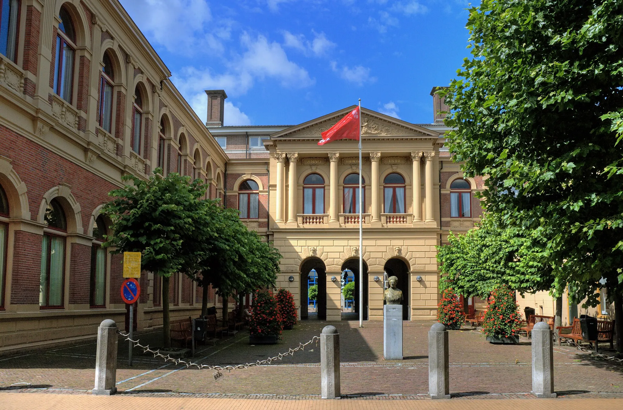 Photo showing: Ingang van De Harmonie (1980), gebouw van de faculteiten Letteren en Rechten van de Rijksuniversiteit Groningen. Hier stond tussen 1856 en 1973 de concertzaal van Groningen (nu in De Oosterpoort). De ingang naar het gebouw doet sterk denken aan façadisme (zij het dat het hele gebouw eerst werd gesloopt) en valt zo niet uit de toon in de Kijk in 't Jatstraat. De  Achter de poort bevindt zich de binnenplaats van het complex met aan de ene kant de standaard flats van de universiteit en aan de andere zijde de Uurwerkersgang.