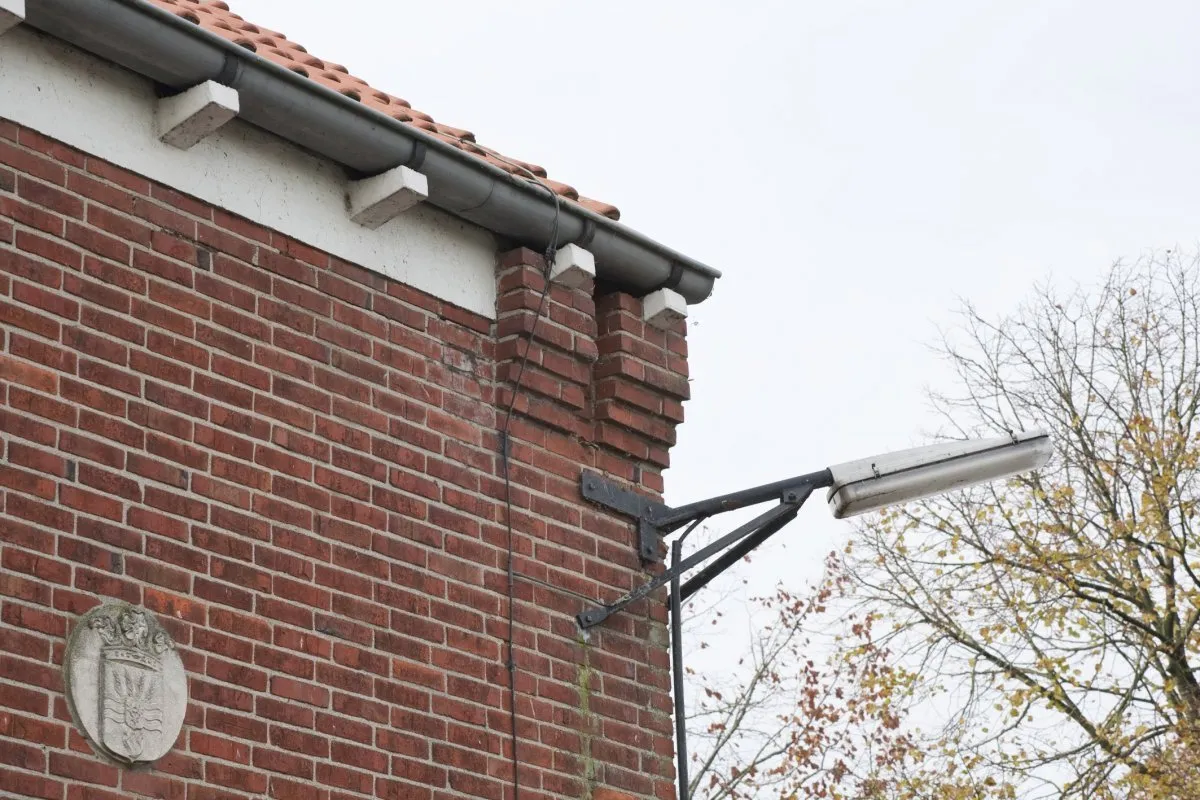 Photo showing: Modelboerderij Johannes Kerkhovenpolder: Detail van rechterdeel voorgevel, gevelbeëindiging bovenkant met uikragend metselwerk en gootklossen, buitenlantaarn en gevelsteen