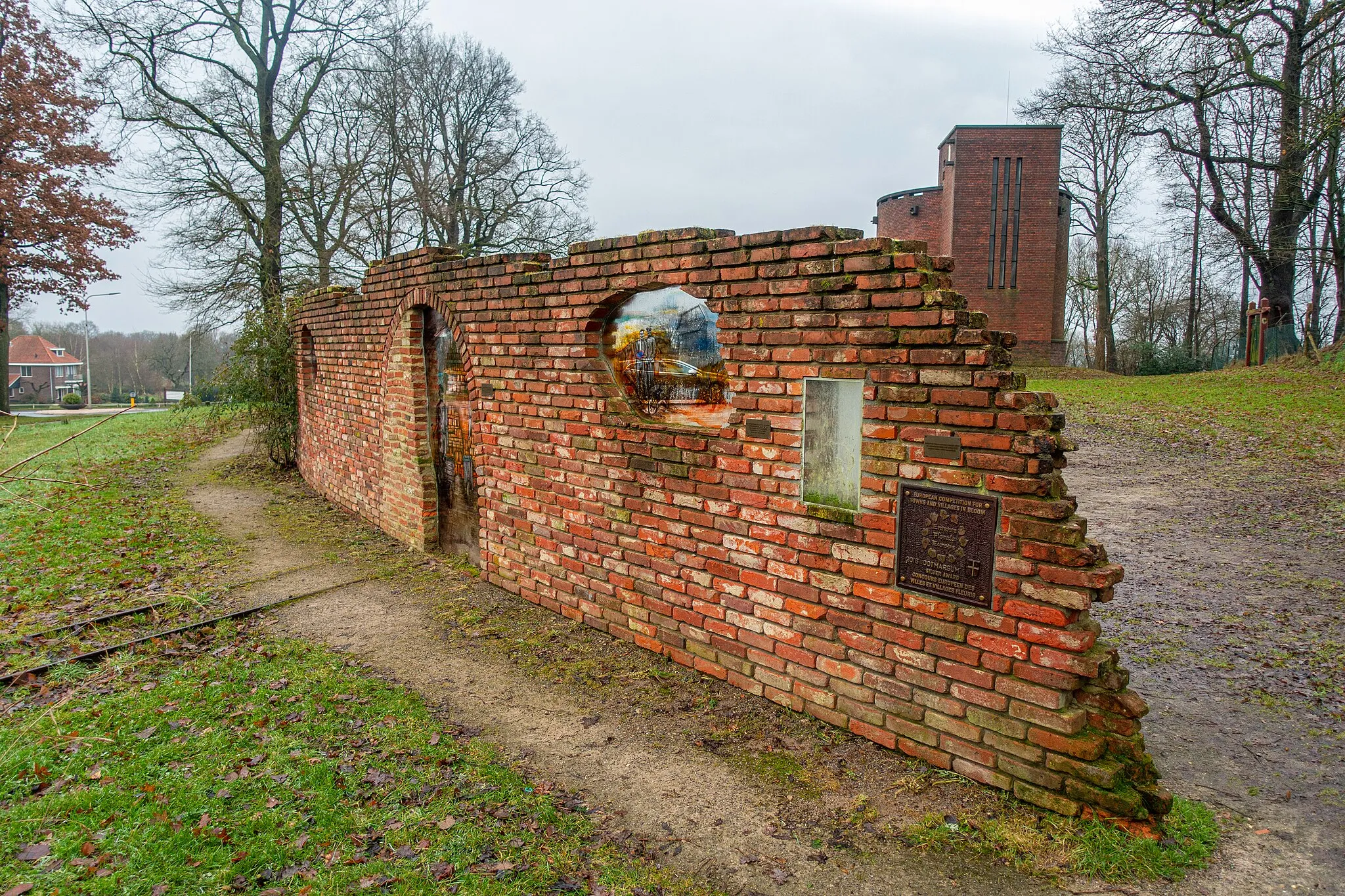 Photo showing: Bakstenen muur met daarin een aantal ramen die de geschiedenis van Ootmarsum tonen. Voor de muur ligt ook een stuk spoor met mijnwagens. Op de achtergrond de watertoren van Ootmarsum.