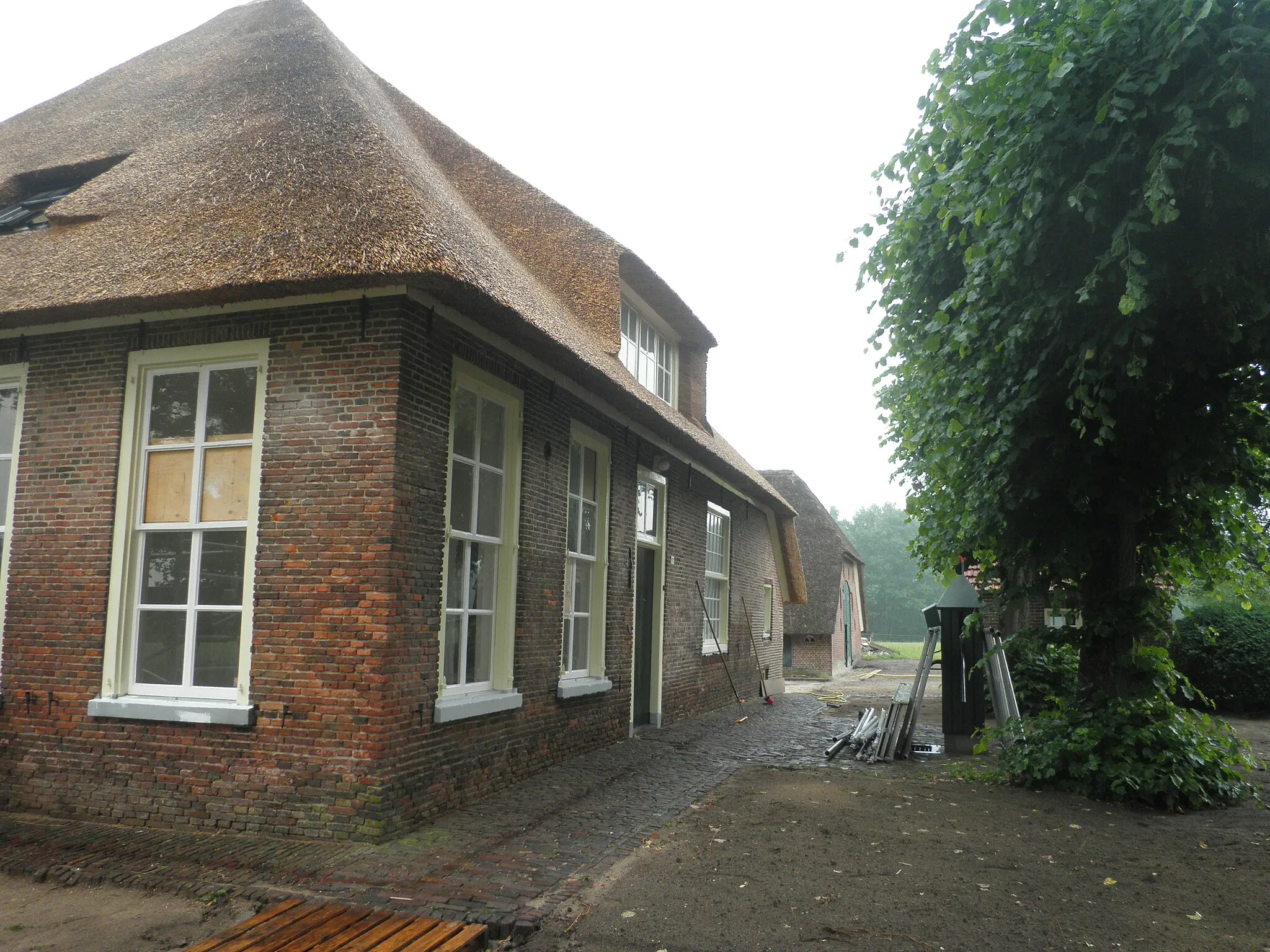 Photo showing: "De Grote Brander": farm house in Okkenbroek, the Netherlands, under thatched hipped roof with a  thatched half hipped roof stable on a T-shaped floor plan. The house has a twelve panel sliding window with half shutters, big eight panel sliding glass windows with hung shutters and a water pump. Nationally listed heritage.