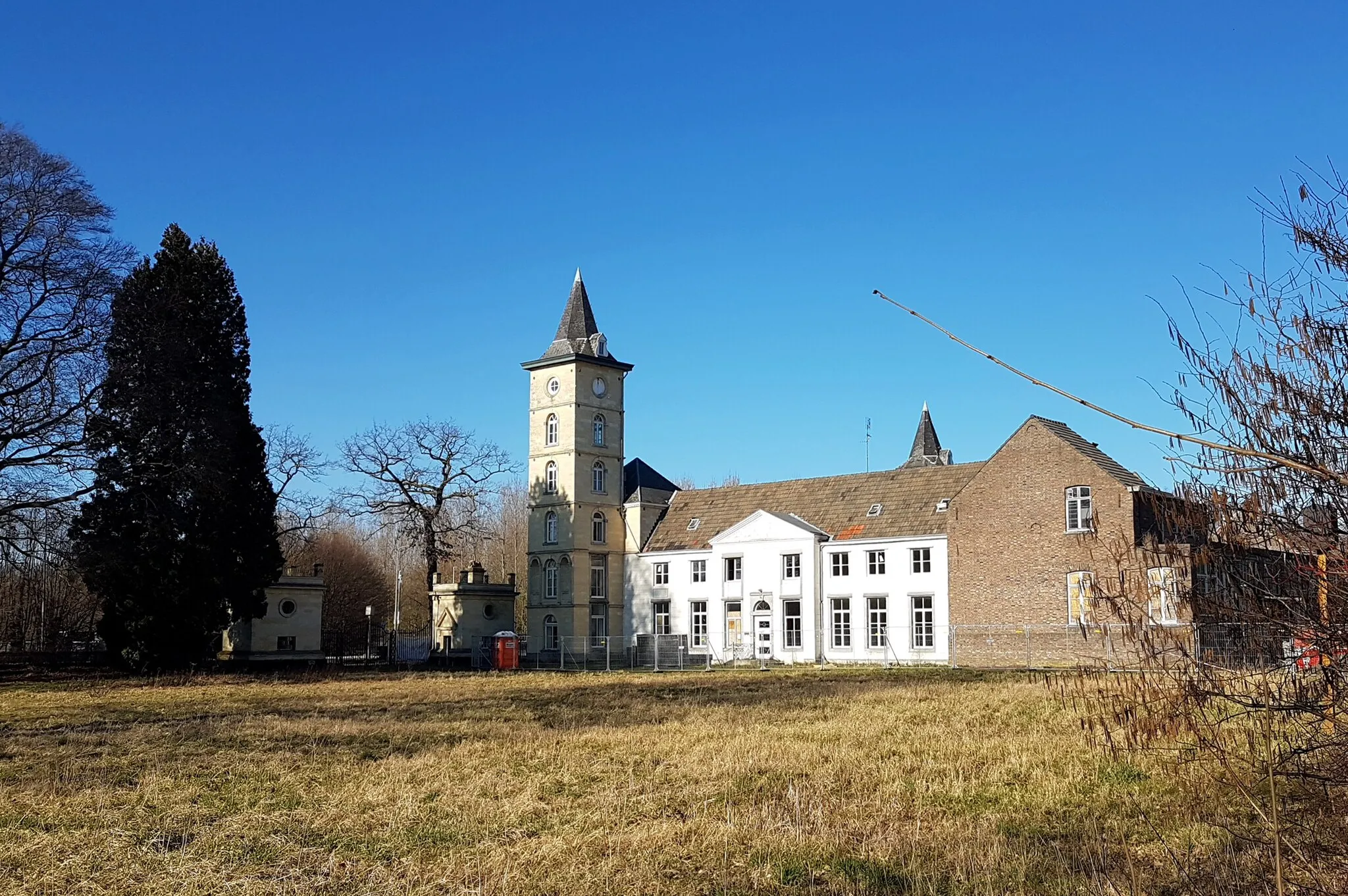 Photo showing: View from the south of the country house La Grande Suisse in Maastricht-Mariënwaard, the Netherlands. The villa was built around 1735 and enlarged with two towers around 1865. From 1875 until 1954 it was used as a Franciscan nunnery and boarding school for girls. In 2018 plans were approved to renovate the derelict building for use as a crematorium. At the time, little remained of the extensive gardens which partly had been taken up by an institution and school for children with special needs.